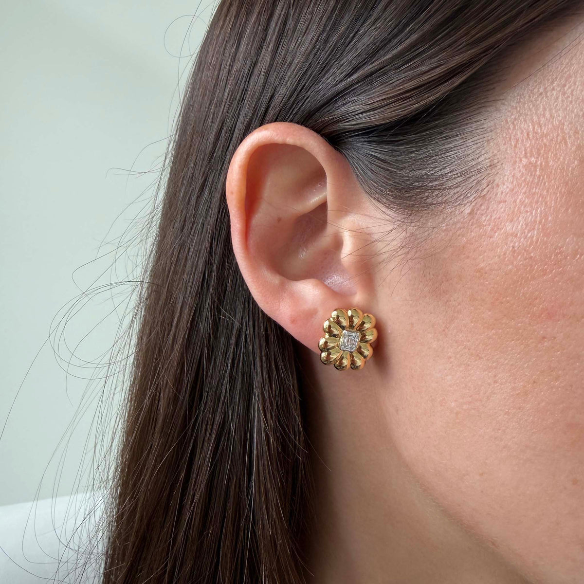 Model wearing an 18K yellow gold diamond flower stud earring, showing its size on the ear.
