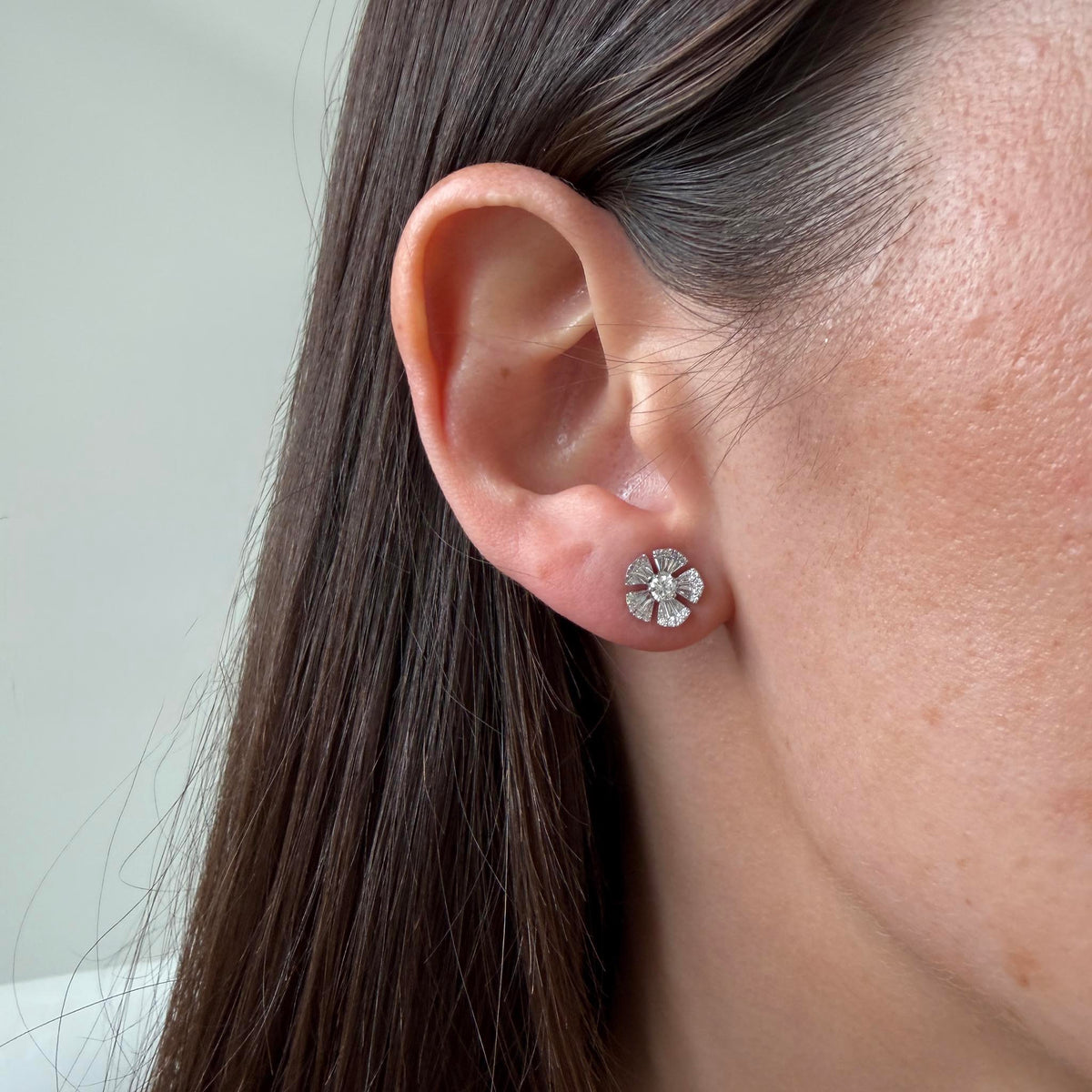 Model wearing a 14K white gold diamond flower stud earring, showing its size on the ear.