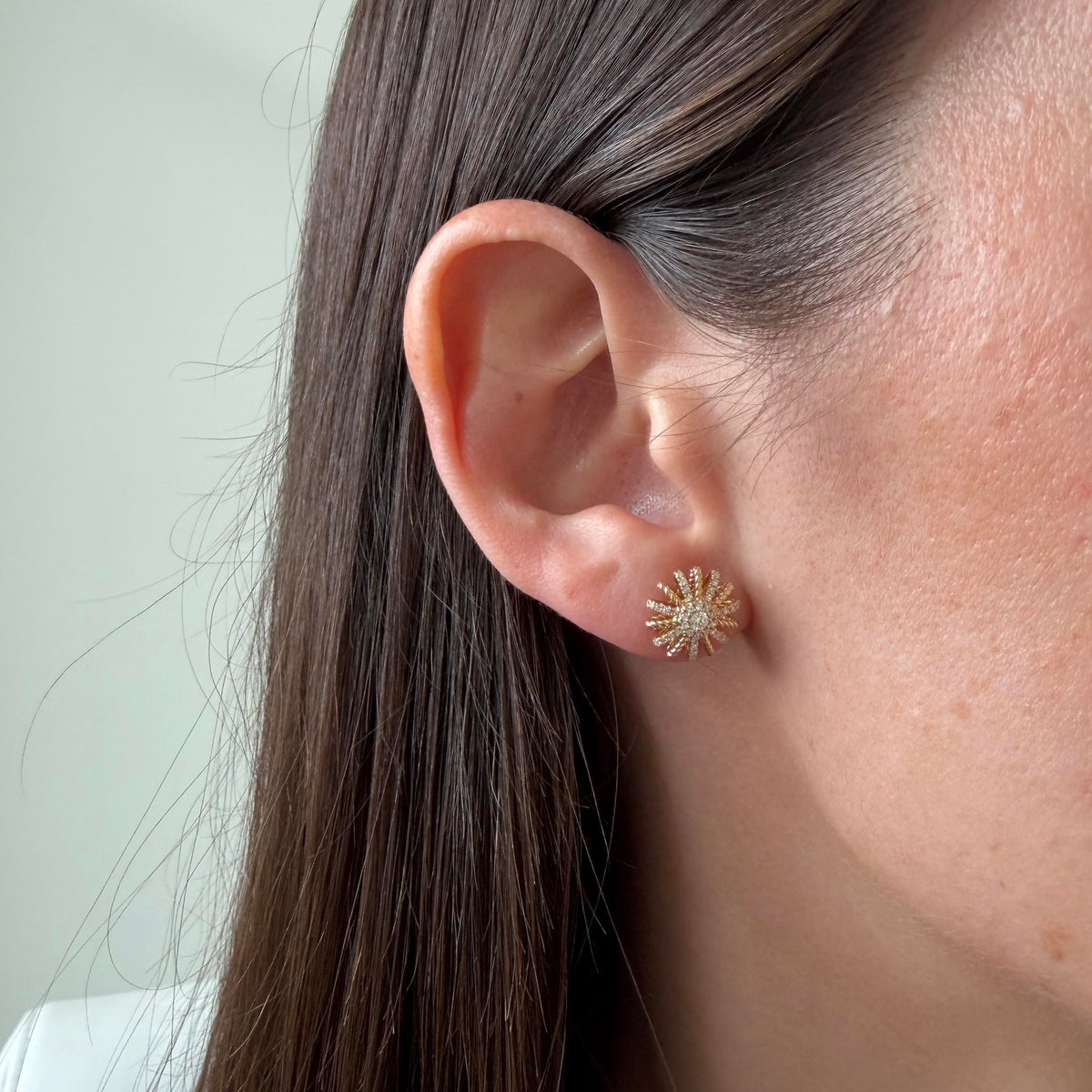 Model wearing a 14K yellow gold diamond starburst stud earring, showing its size on the ear.
