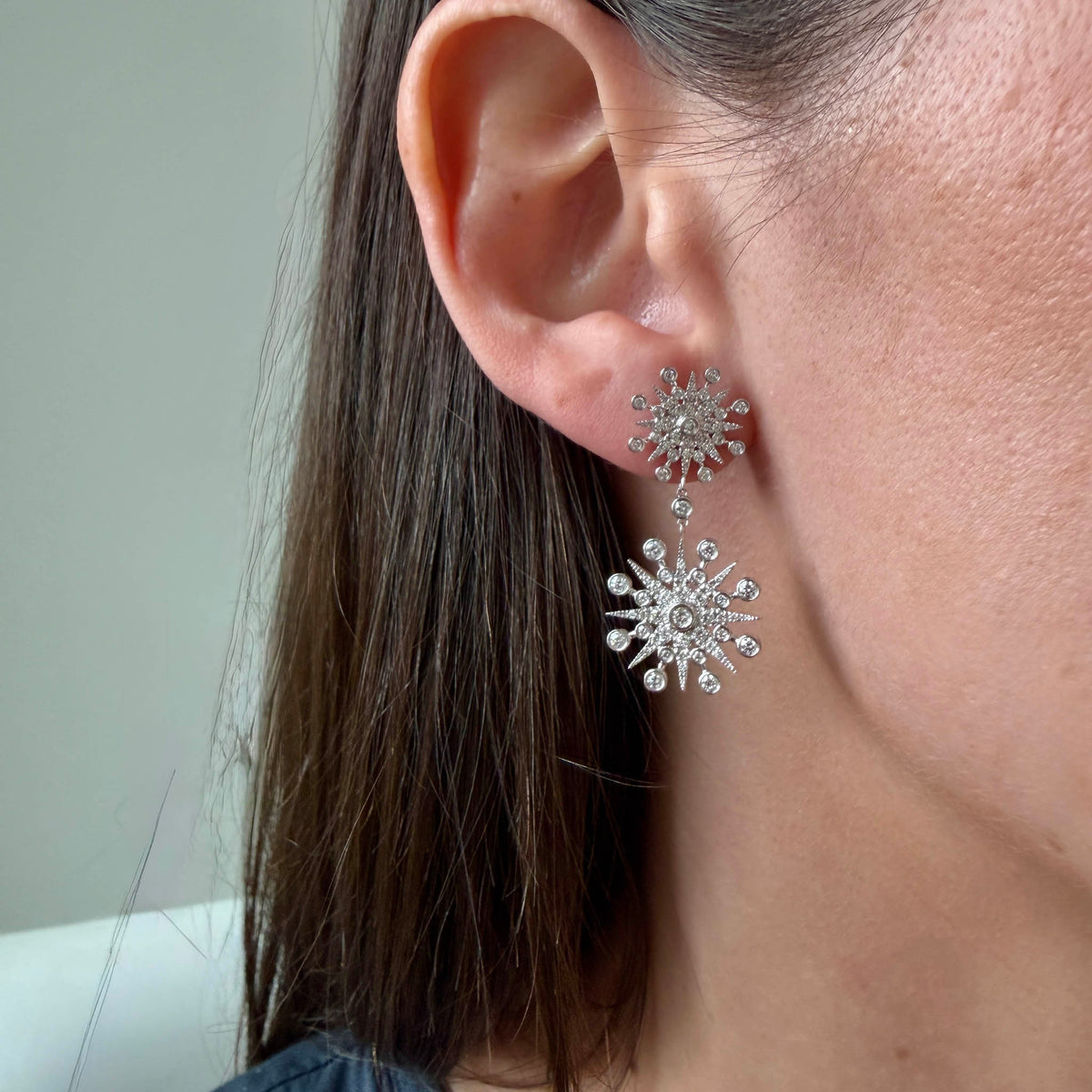 Model wearing a 14K white gold diamond starburst drop earring, showing its length below the earlobe.