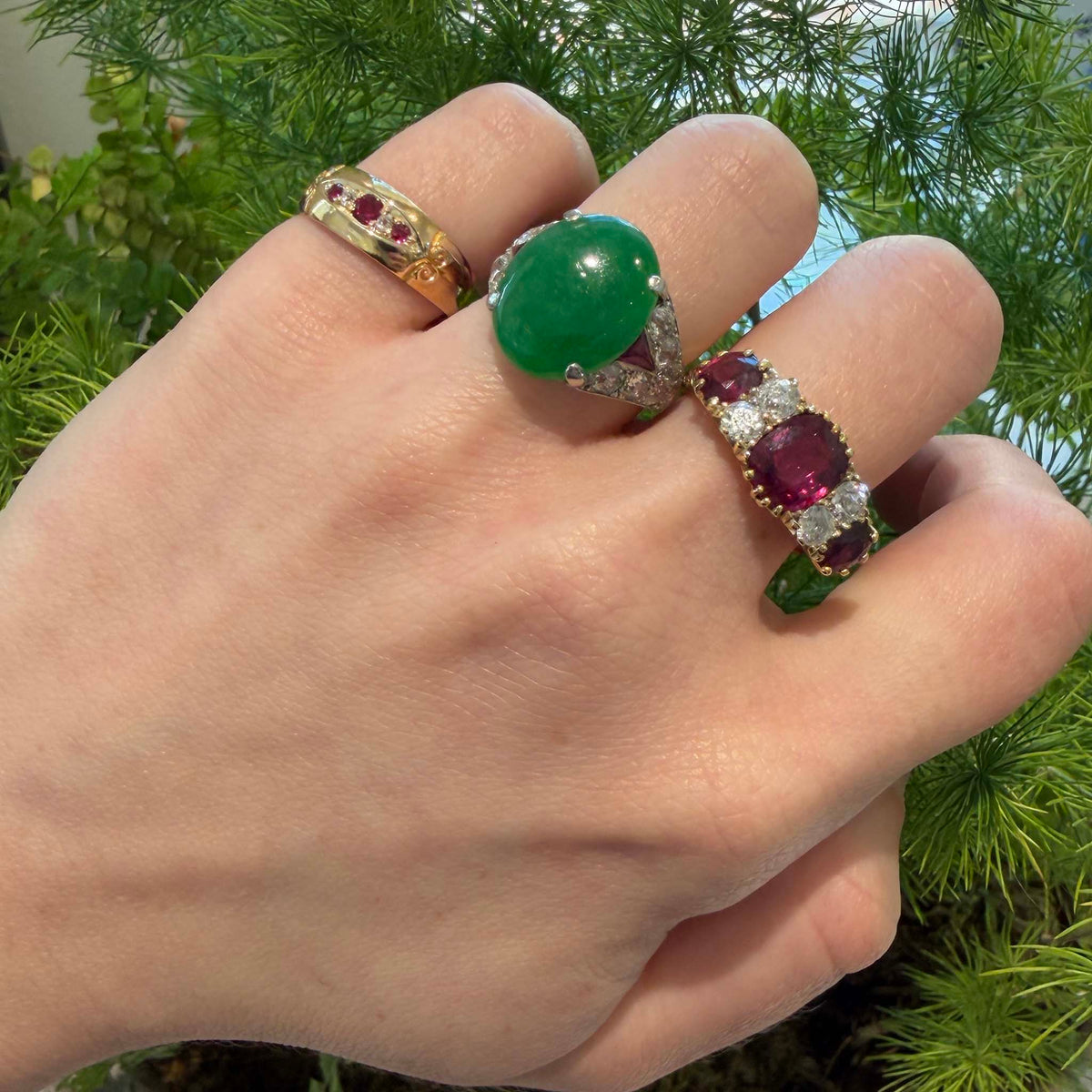 Green jadeite, diamond and ruby platinum ring worn on the middle finger beside two ruby rings.