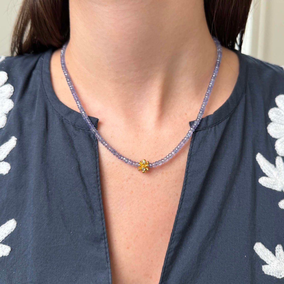 Model wearing a Tippy Stern lavender-blue tanzanite beaded necklace with a stone-set yellow gold rondelle centered at the front.