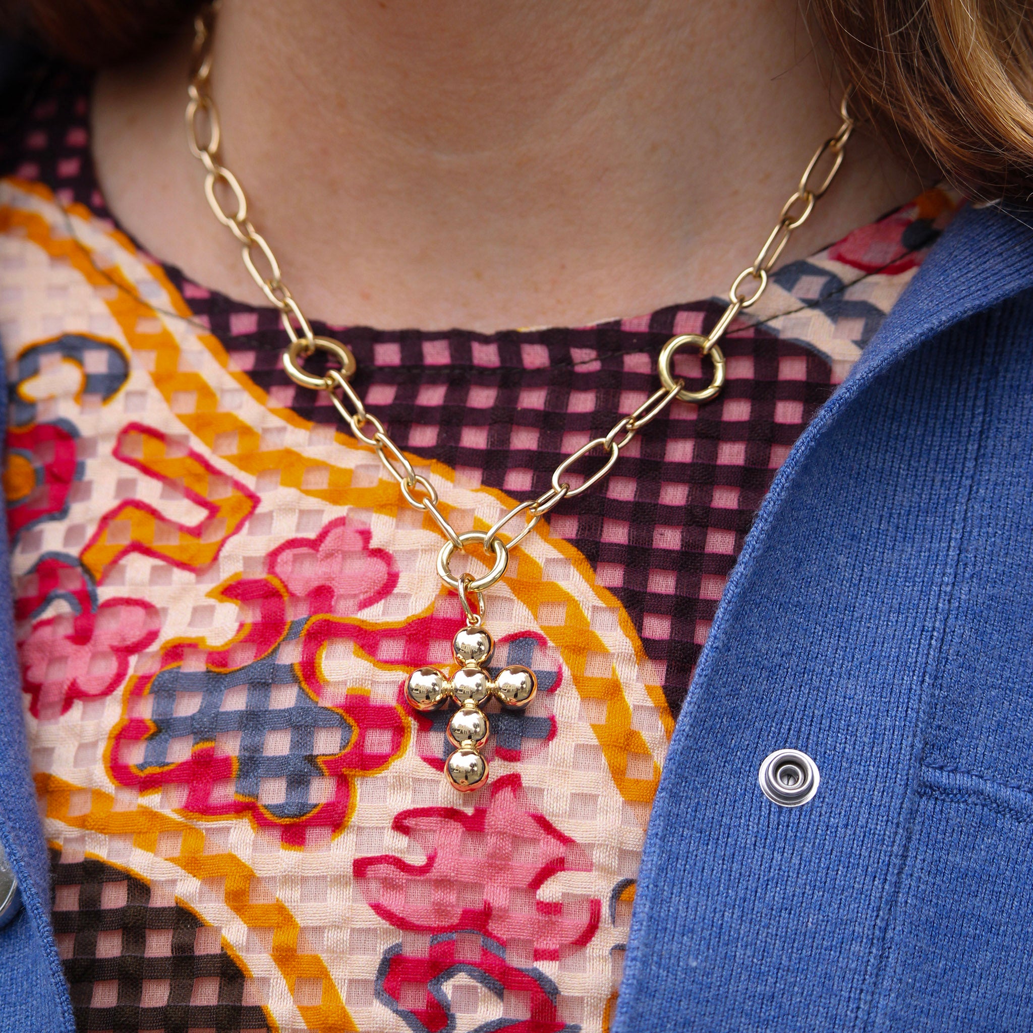 Close-up of a person wearing a gold chain necklace with a cross pendant, against a colorful patterned background.