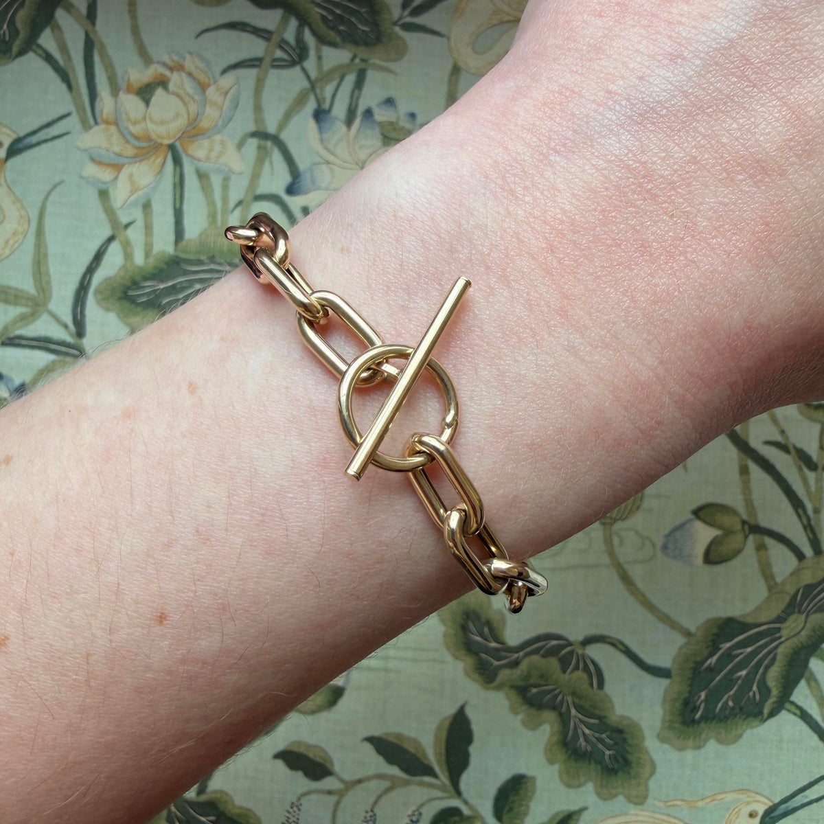 14K yellow gold paperclip link bracelet worn on the wrist, showing the circular toggle clasp and polished bar.