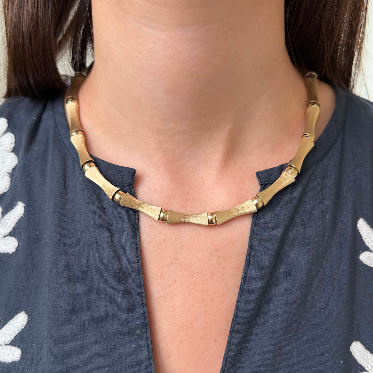 Model wearing a 14K yellow gold bamboo link necklace, showing its fit along the neckline.