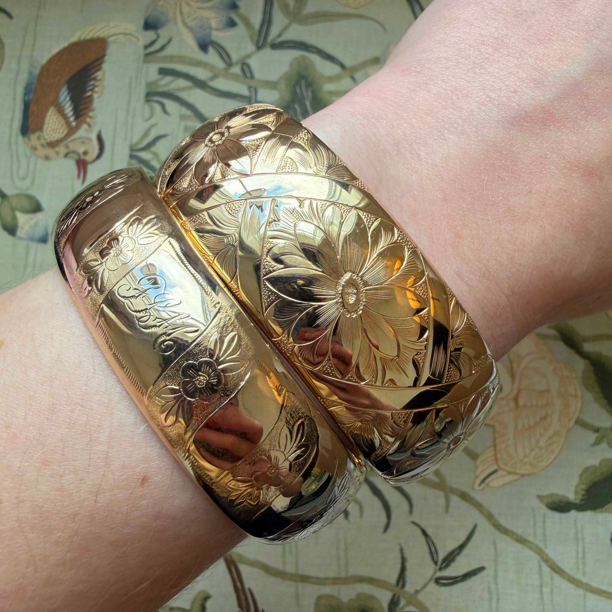 Vintage engraved floral pattern wide gold-filled bangle worn on a wrist beside another engraved bangle.