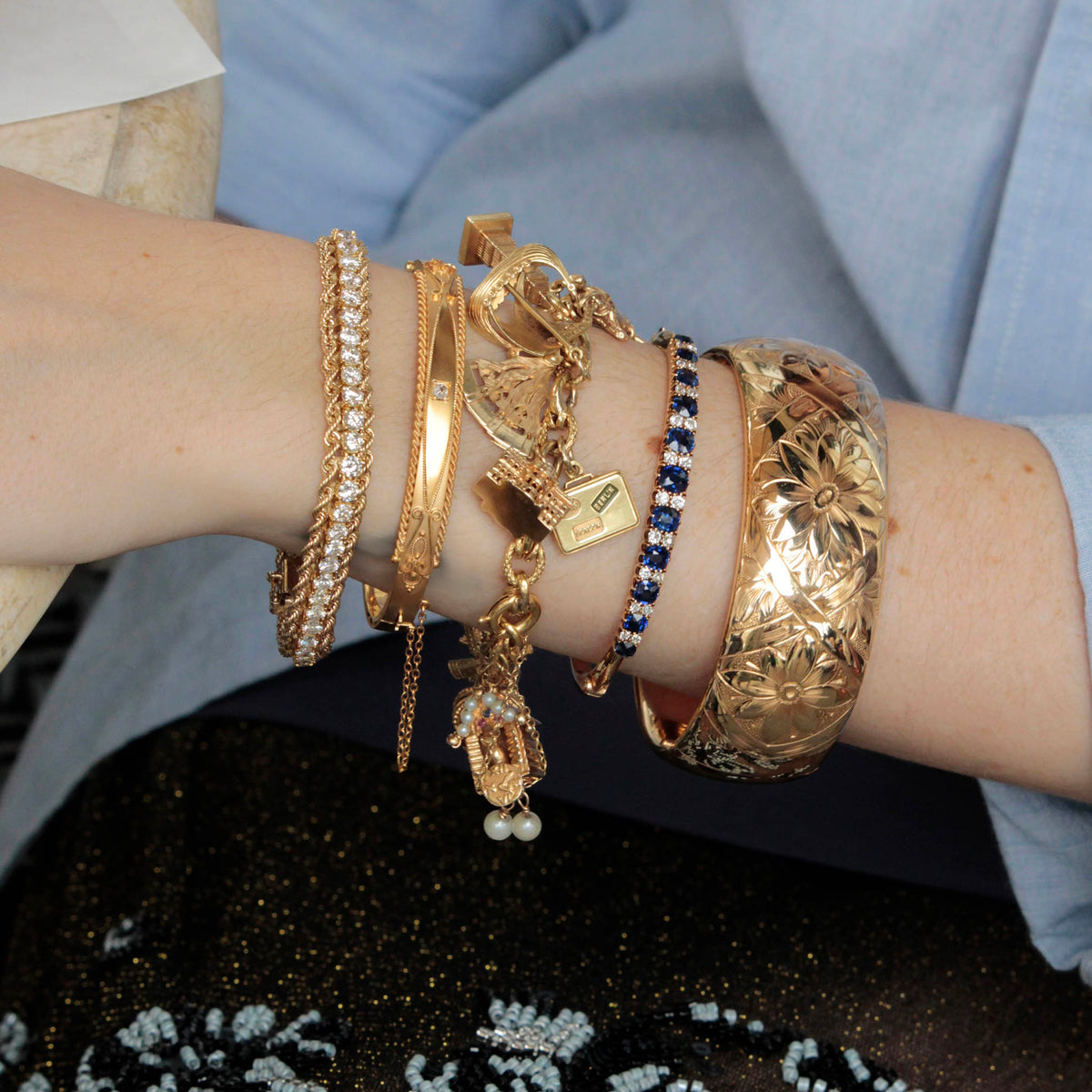 Victorian diamond gold bangle worn between a diamond bracelet and a gold charm bracelet in a layered wrist stack.