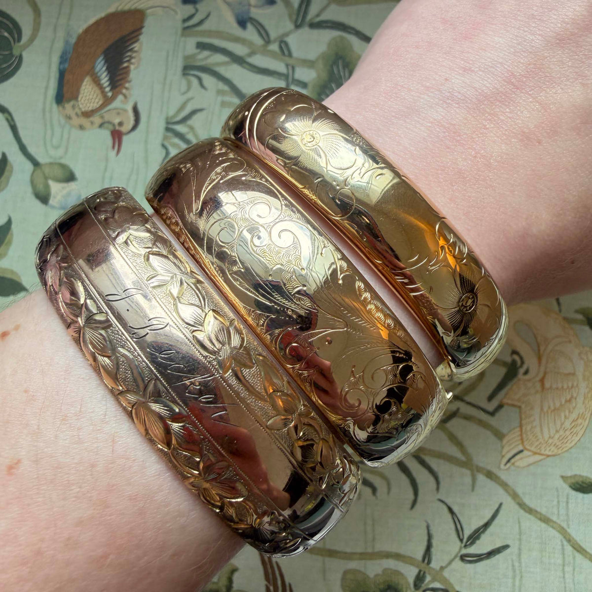 Vintage engraved floral pattern wide gold-filled bangle worn on a wrist beside two other engraved bangles.