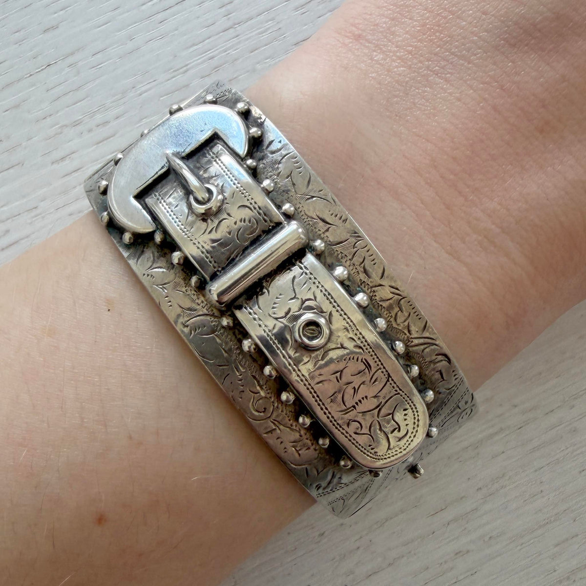 Victorian sterling silver buckle bangle worn on a wrist, showing the wide band and engraved buckle design.