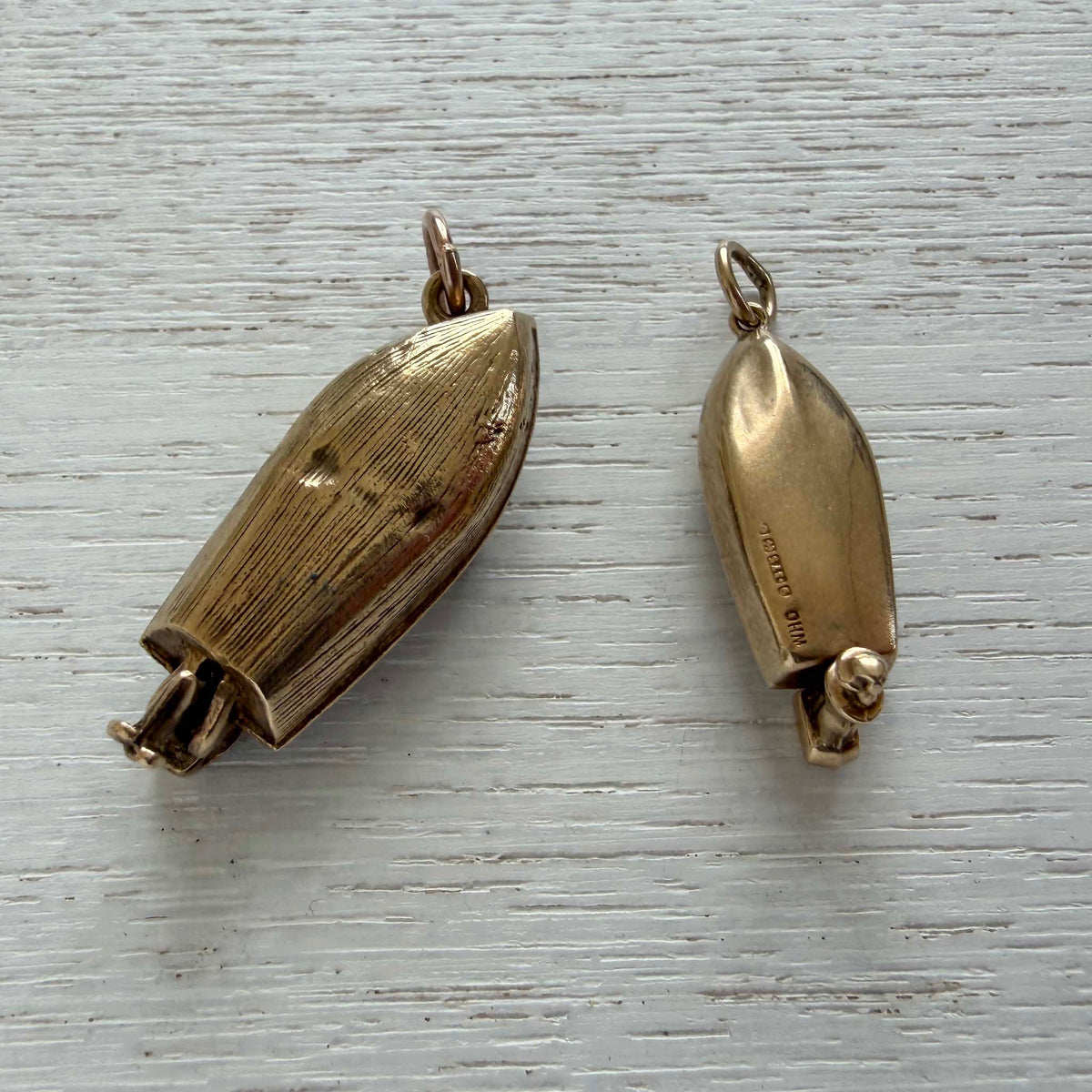 Underside view of a vintage gold speedboat charm beside a larger motorboat charm on white wood.