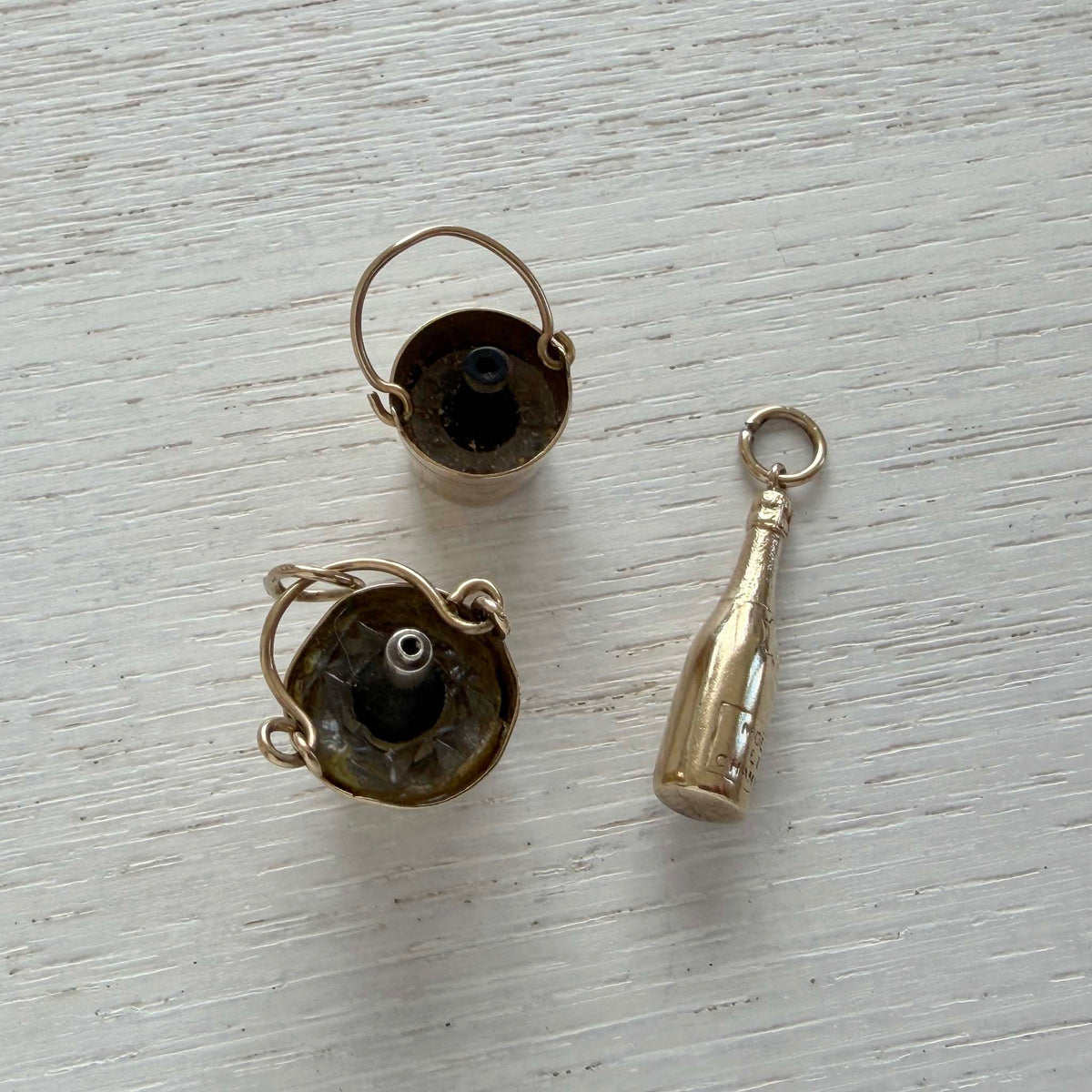 Top view of two gold champagne bucket charms showing the bottles inside, beside a gold champagne bottle charm.