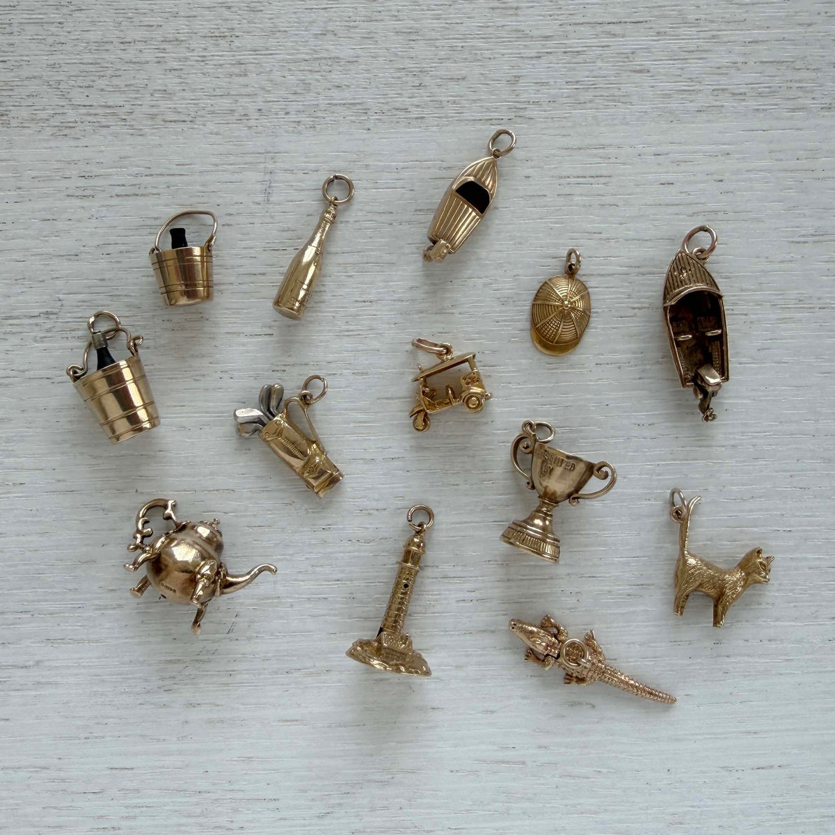 Vintage gold champagne bucket charm among assorted gold charms, including boats, a trophy, a teapot, and a cat.