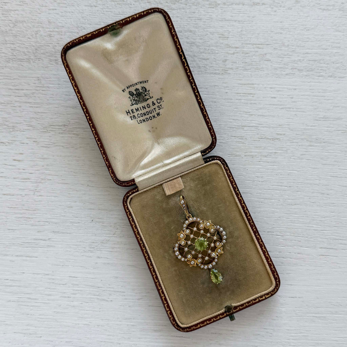 Victorian peridot and seed pearl gold pin/pendant displayed in an open antique Heming & Co. jewelry box.