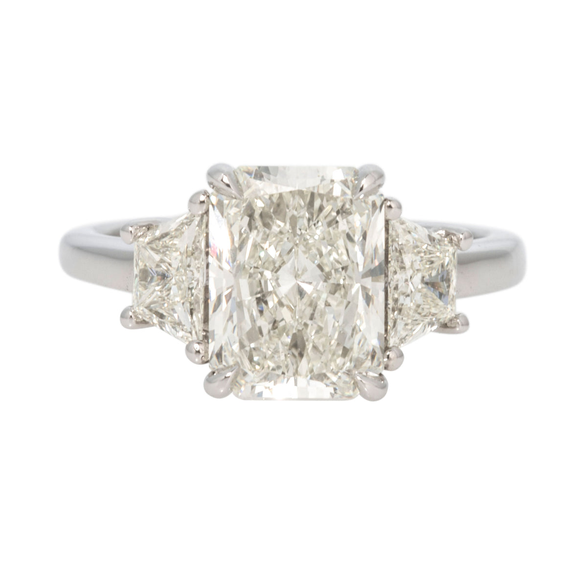 Platinum three-stone ring with a radiant-cut center diamond and trapezoid side diamonds, viewed from the front.