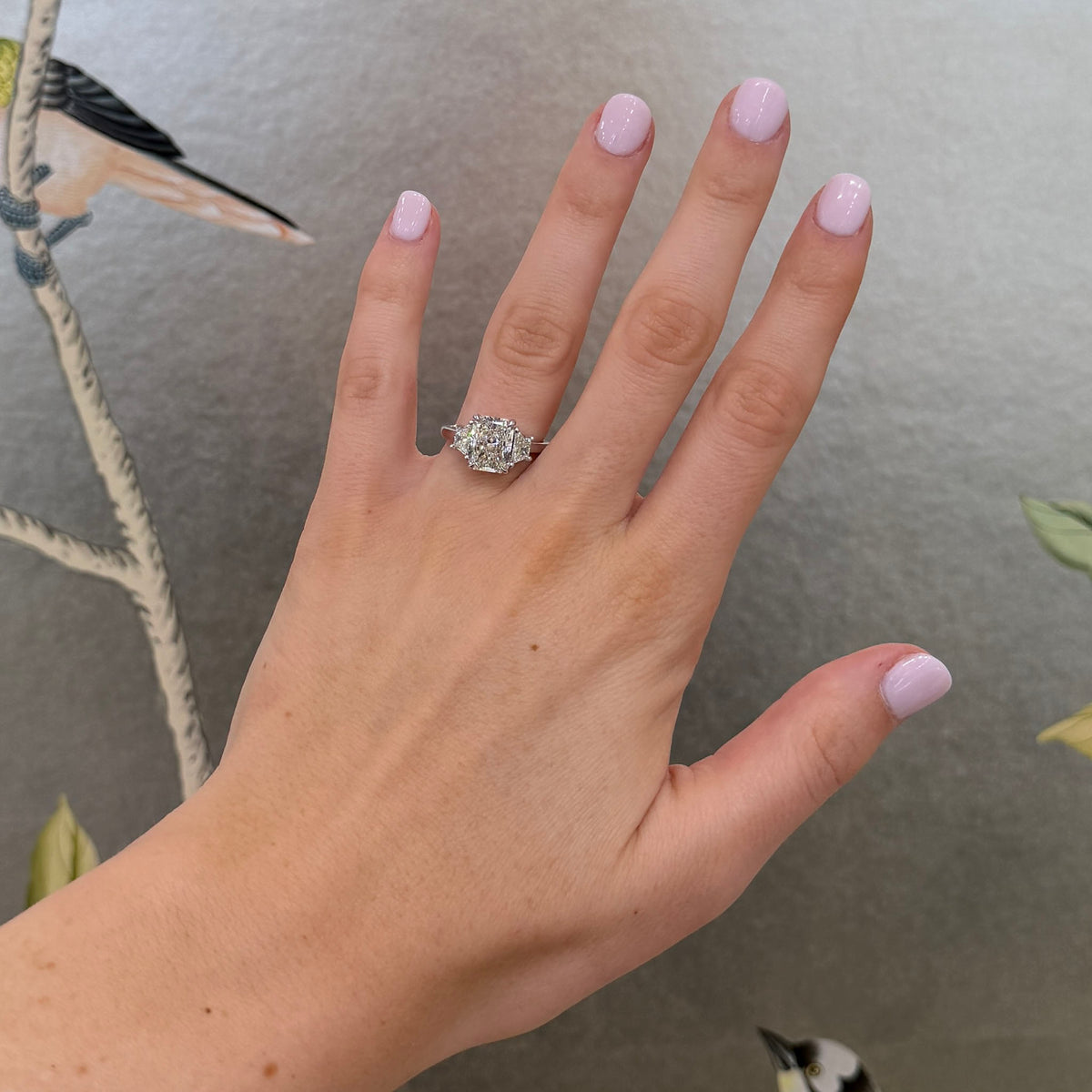 Radiant-cut diamond three-stone platinum ring with trapezoid side diamonds worn on a hand.