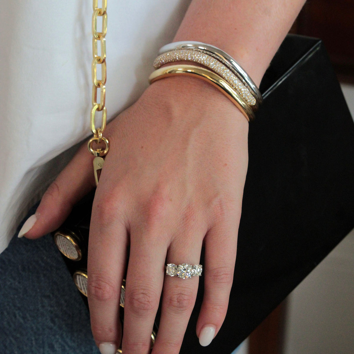 hand on purse with three-stone diamond ring styled with a triple stack of Paul Morelli bangles