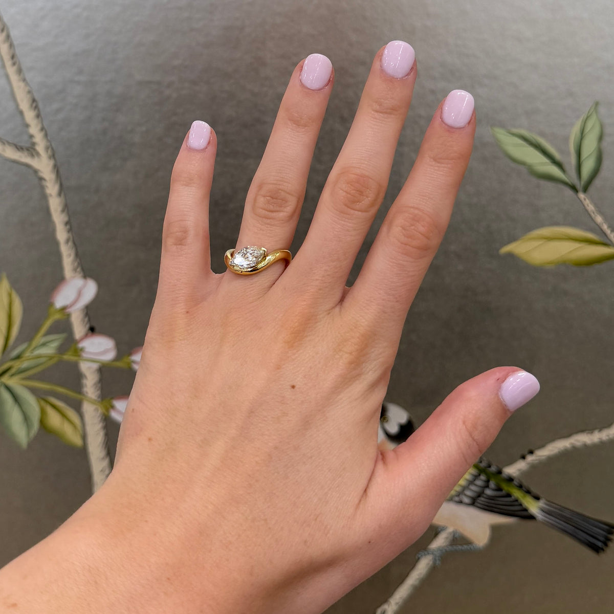 Marquise diamond solitaire ring with an 18K yellow gold wave band worn on the ring finger.
