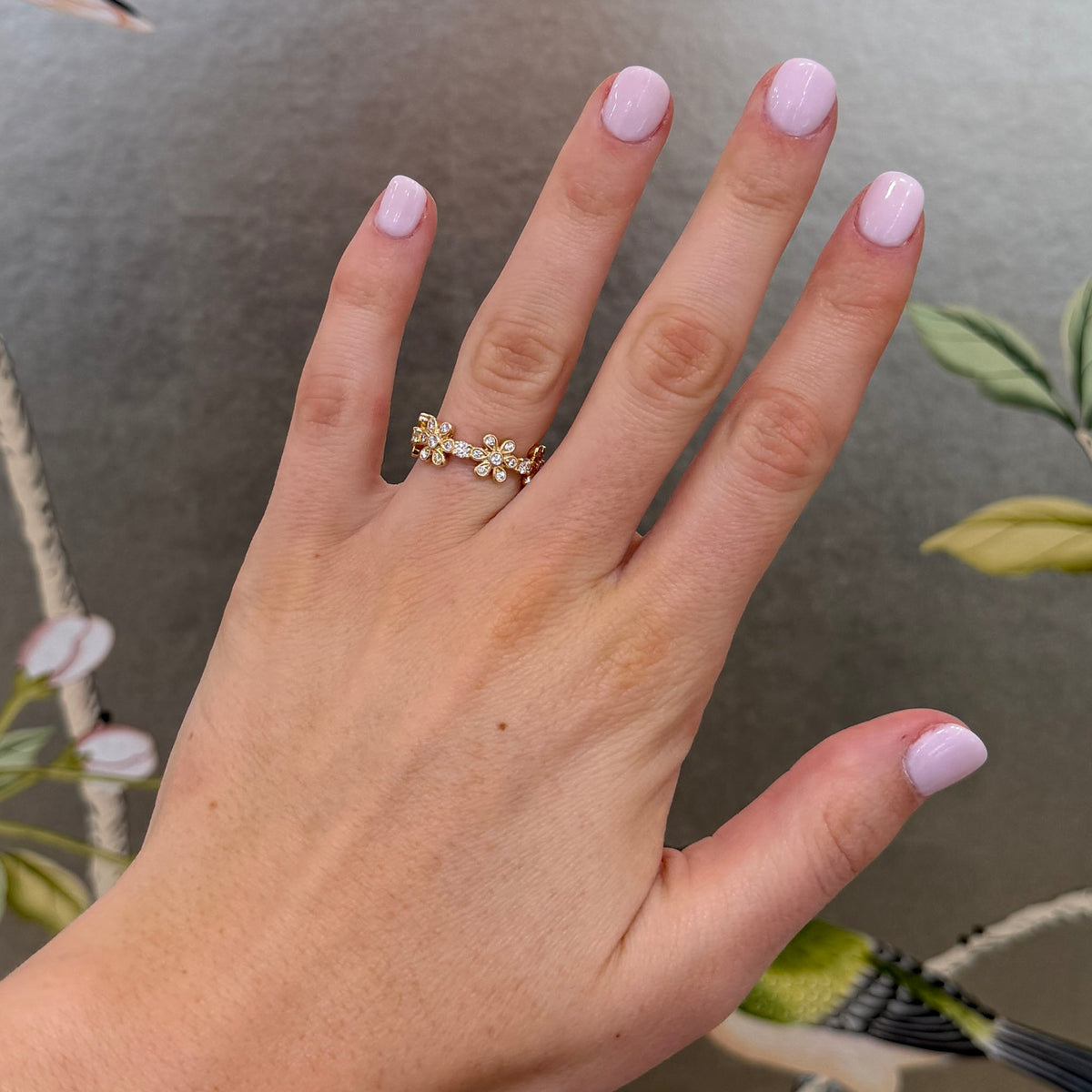 Diamond floral eternity band in 14K yellow gold worn on a hand, showing the flower motifs and scale.