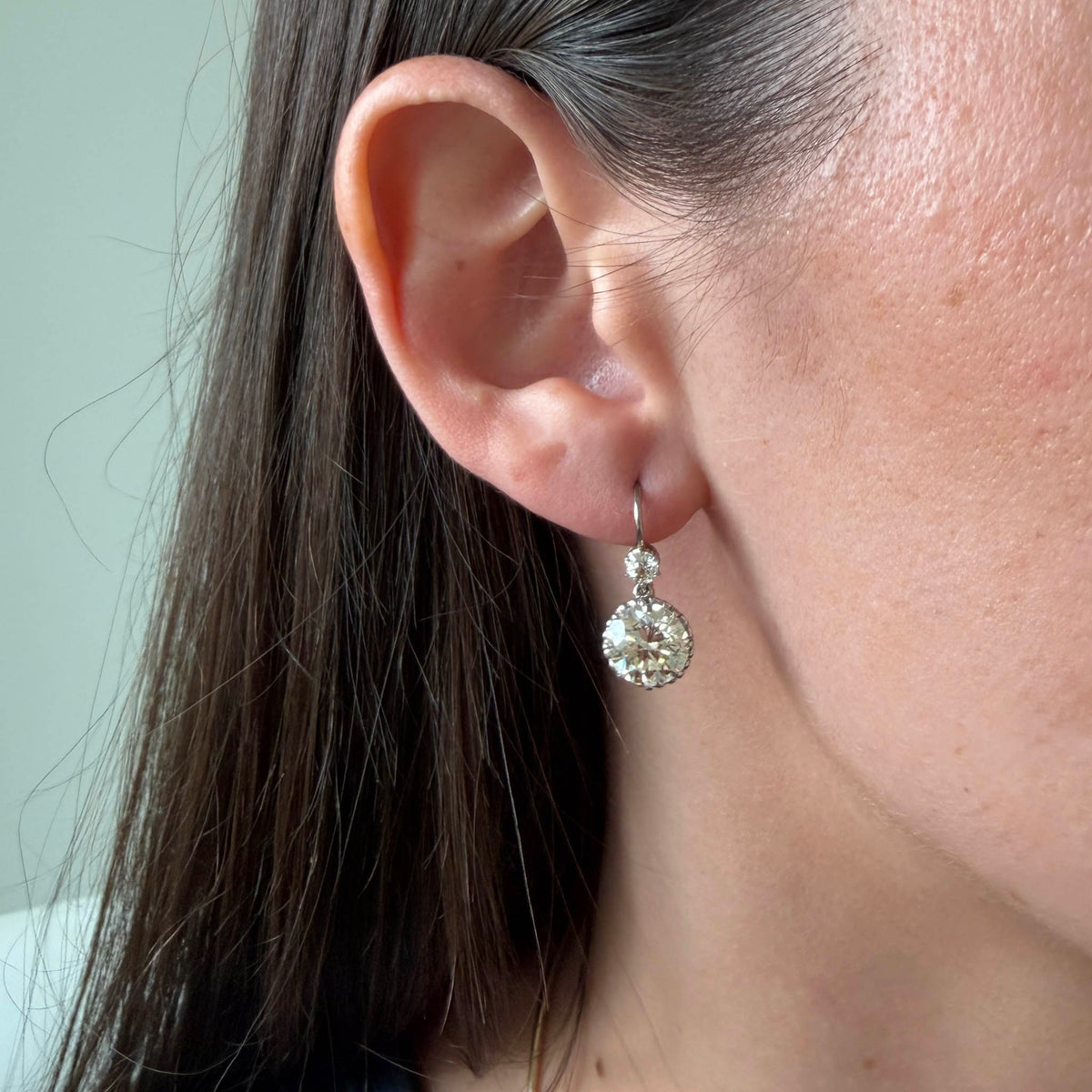 Victorian-style platinum double drop diamond earring worn on the ear to show its size and length.