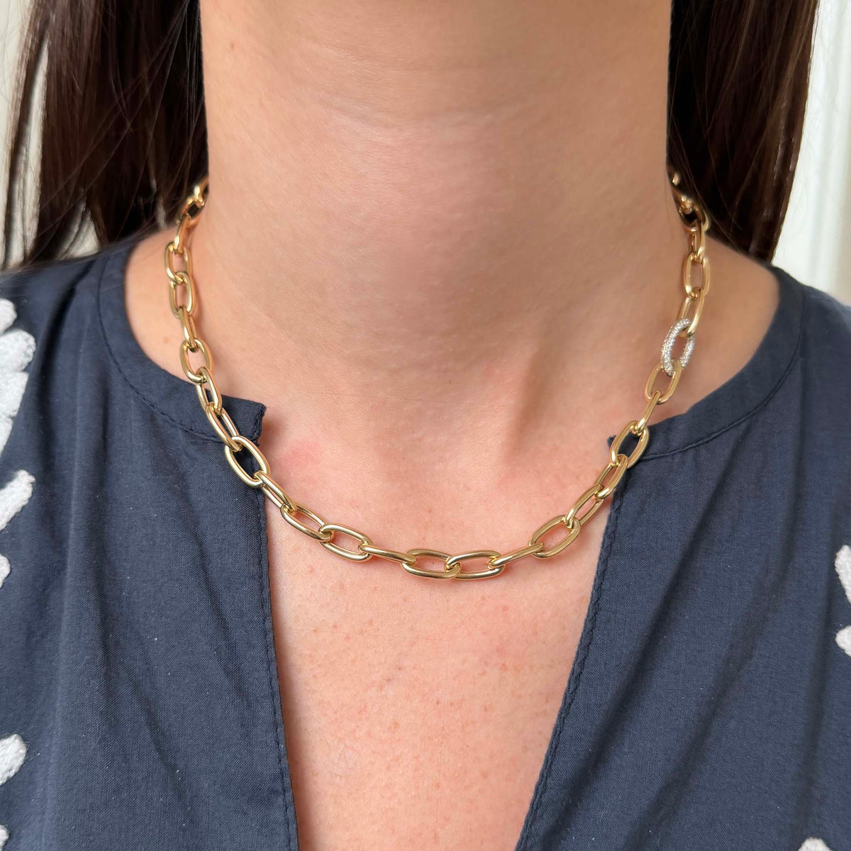 Model wearing a 14K yellow gold oval link necklace with a diamond pavé white gold accent link positioned to one side.