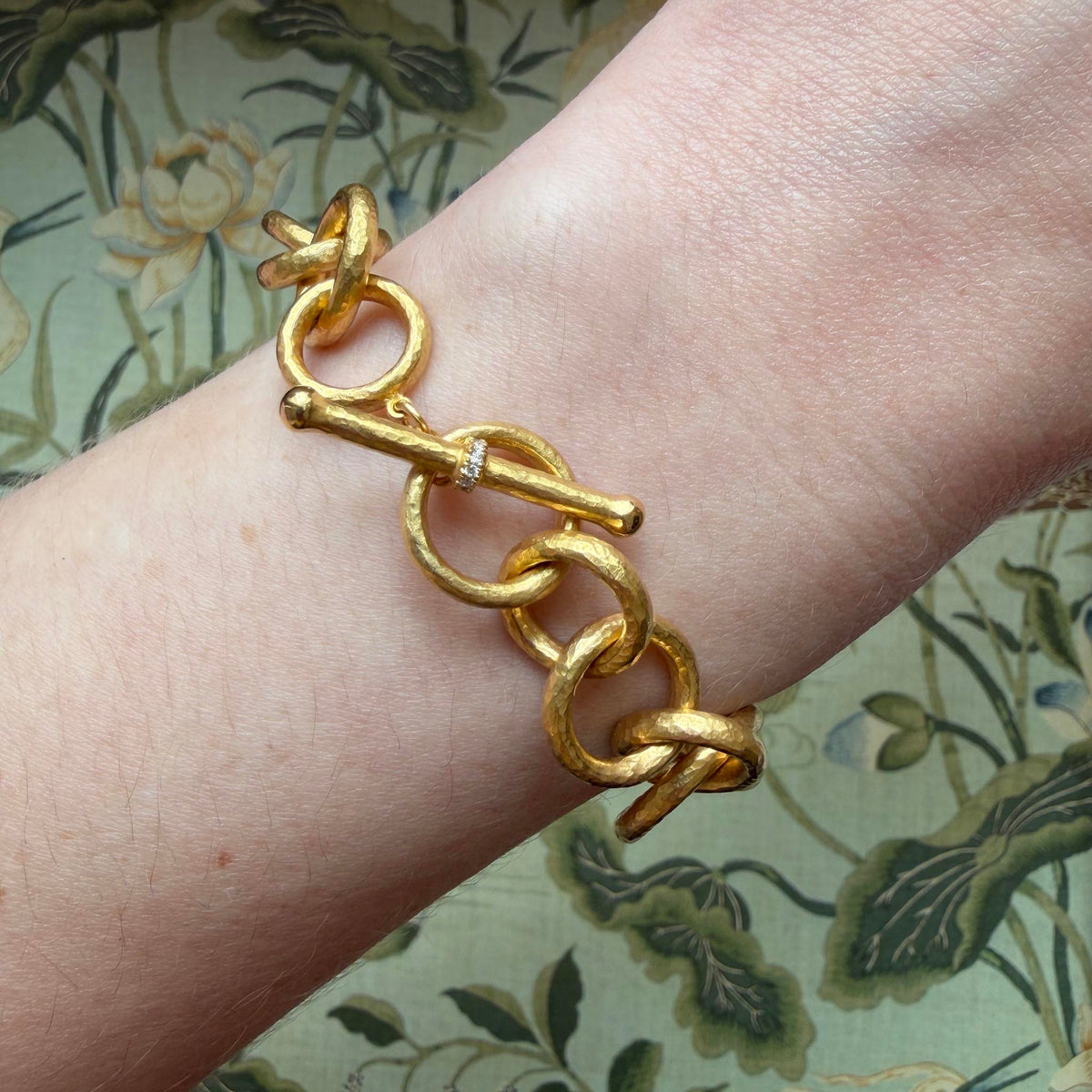 14K yellow gold hammered link bracelet worn on the wrist, showing the toggle clasp with pavé diamond accents.