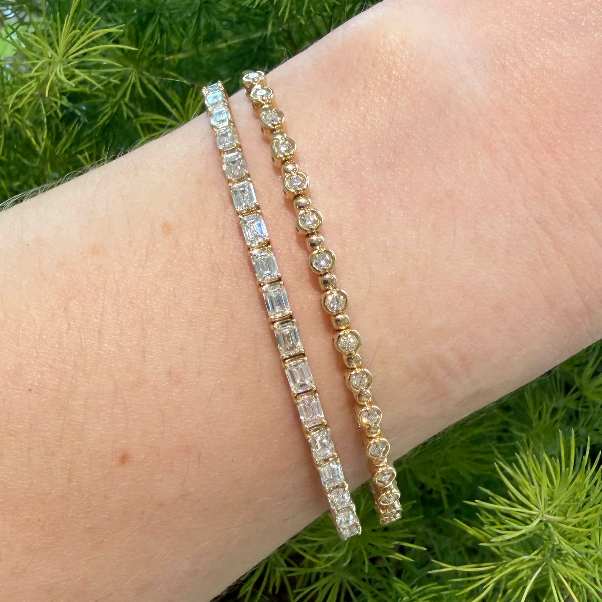 Emerald-cut diamond bangle in 14K yellow gold worn on the wrist beside a round bezel-set diamond bracelet.⠋