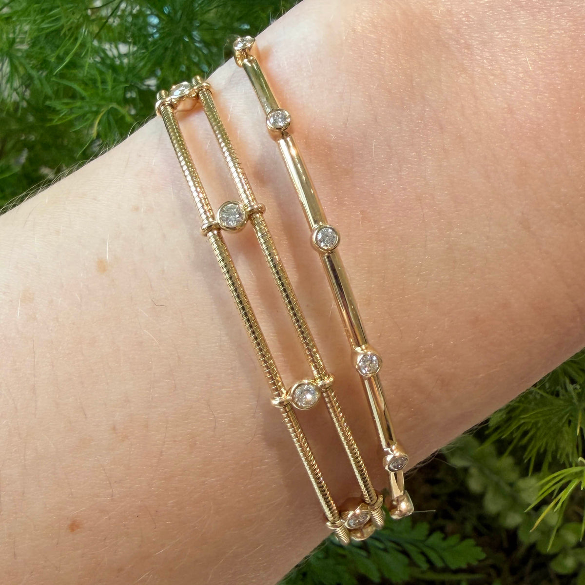 Double-row diamond station bangle in 14K yellow gold worn on the wrist beside a slim single-row diamond bangle.