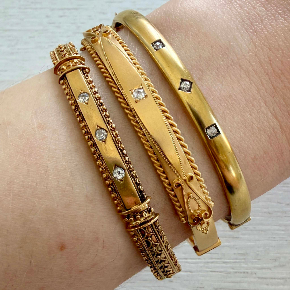 Victorian Etruscan Revival three-diamond gold bangle worn on a wrist alongside two other gold bangles.