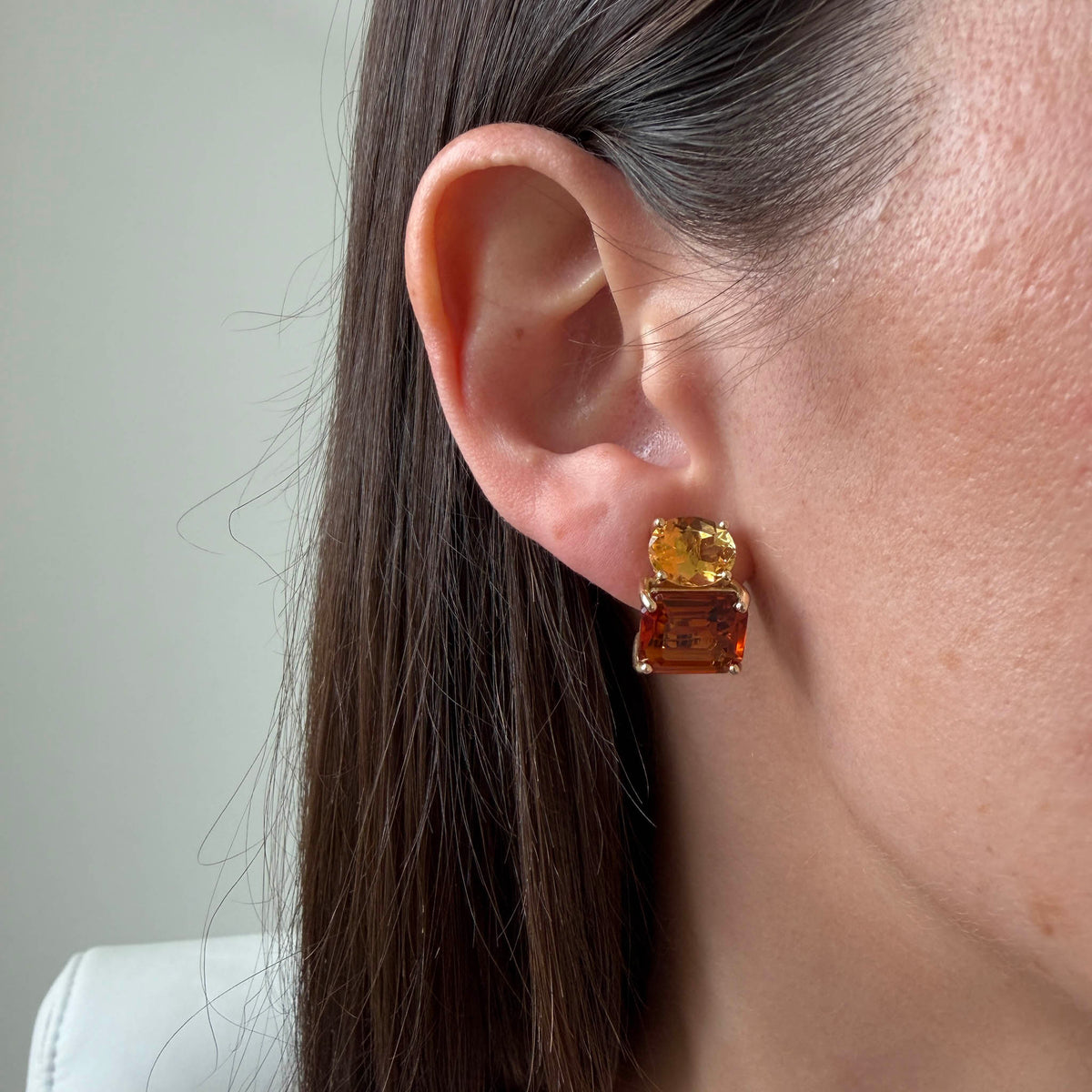 Two-stone citrine earring worn on the ear, showing an oval light citrine above a rectangular dark citrine in 14K yellow gold.