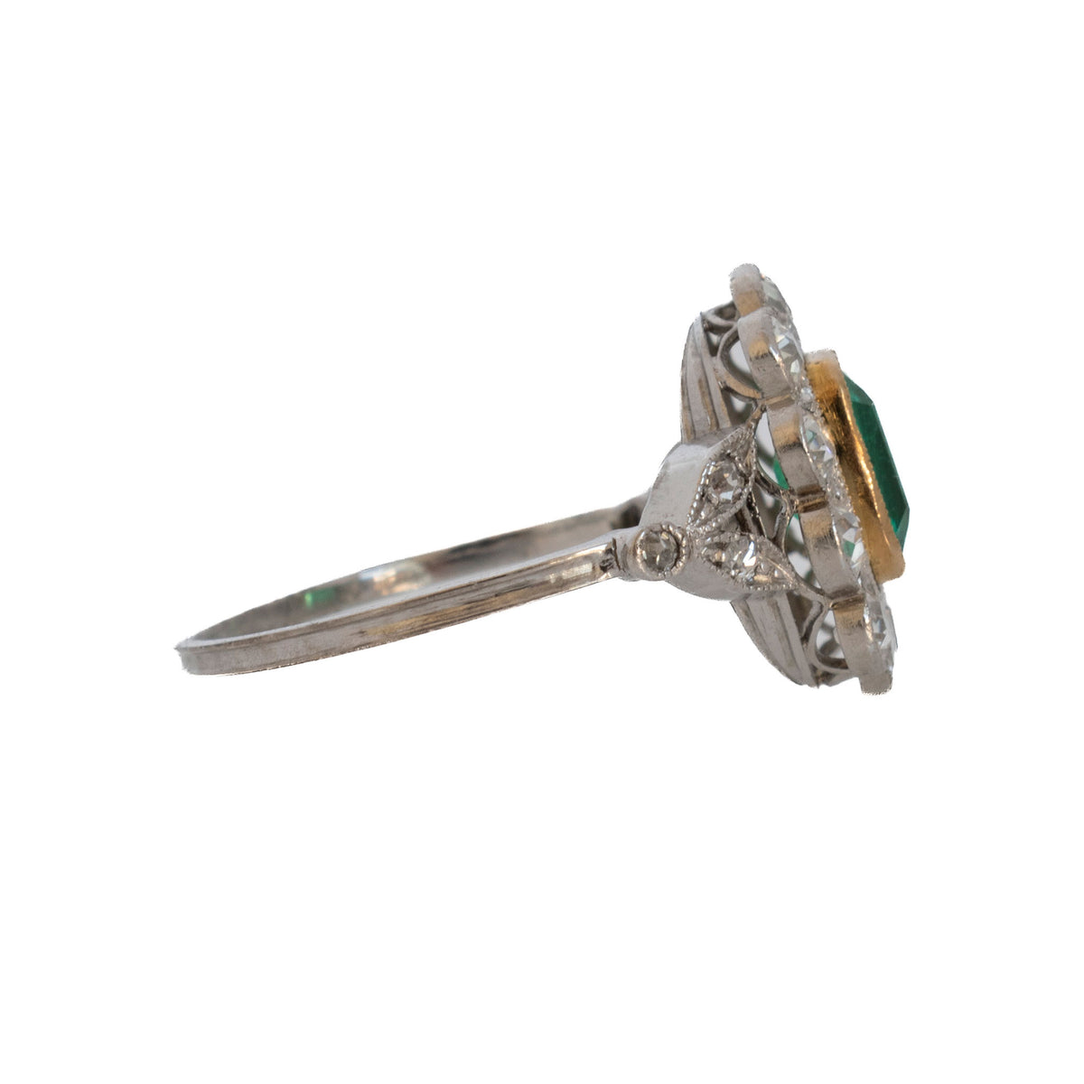 Edwardian emerald and diamond cluster ring showing the raised openwork setting and diamond-set shoulders.