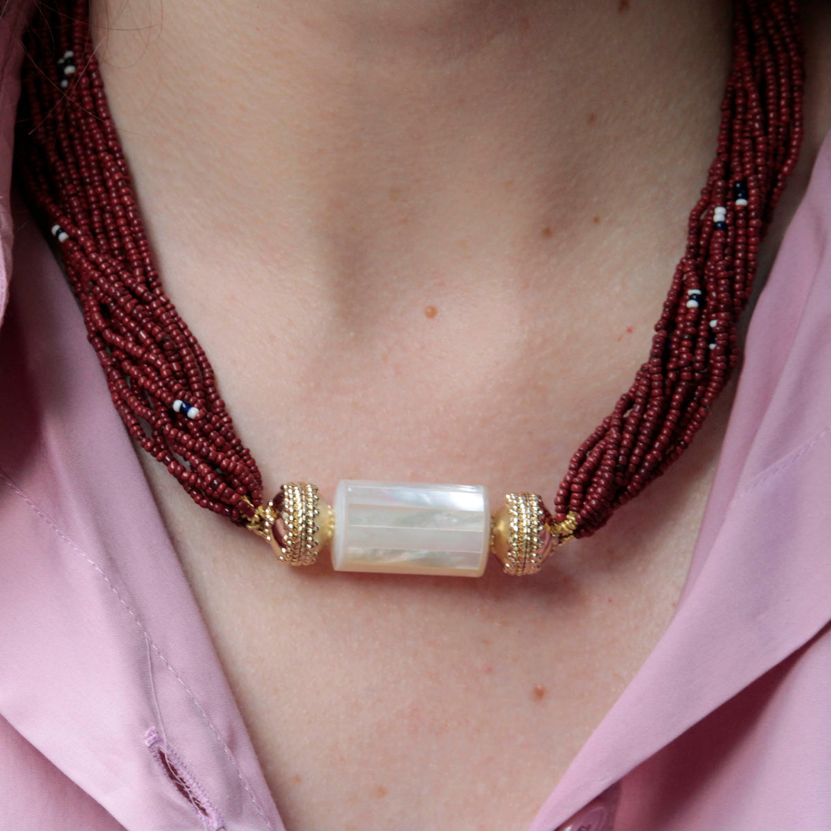 Model in a pink shirt wearing Clara Williams Mother-of-Pearl Tube Centerpiece on Maroon Ivory Coast Glass Multi-Strand Necklace.