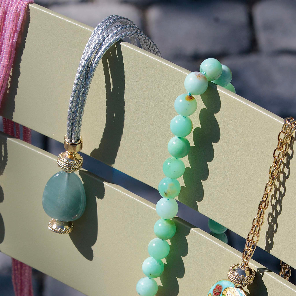 Clara Williams Wellington Braided Silver Leather Necklace with Aquamarine Oblong Centerpiece draped over a light green chair