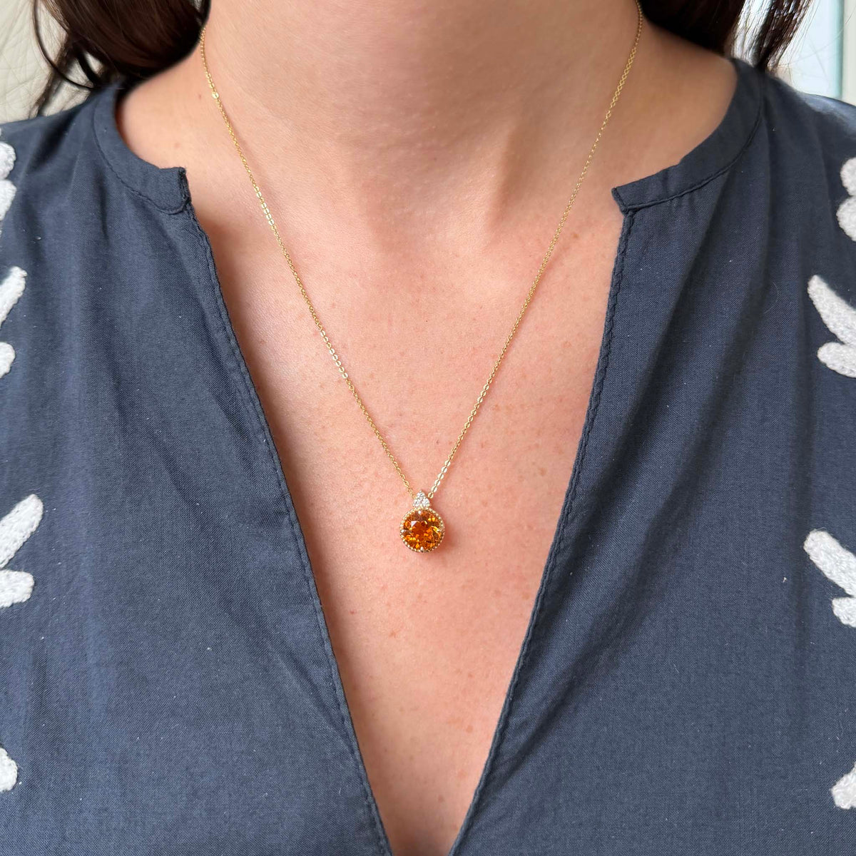 Citrine and diamond pendant necklace in 14K yellow gold worn below the collarbone, showing its round golden-orange gemstone and delicate cable chain.