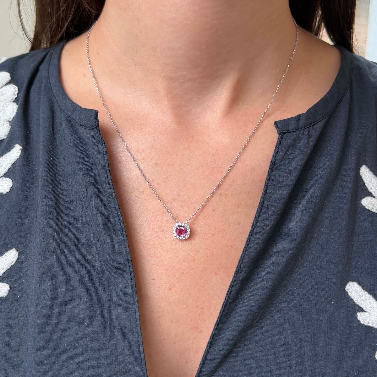 ink sapphire and diamond halo pendant necklace in 18K white gold worn below the collarbone, showing its size and delicate cable chain.
