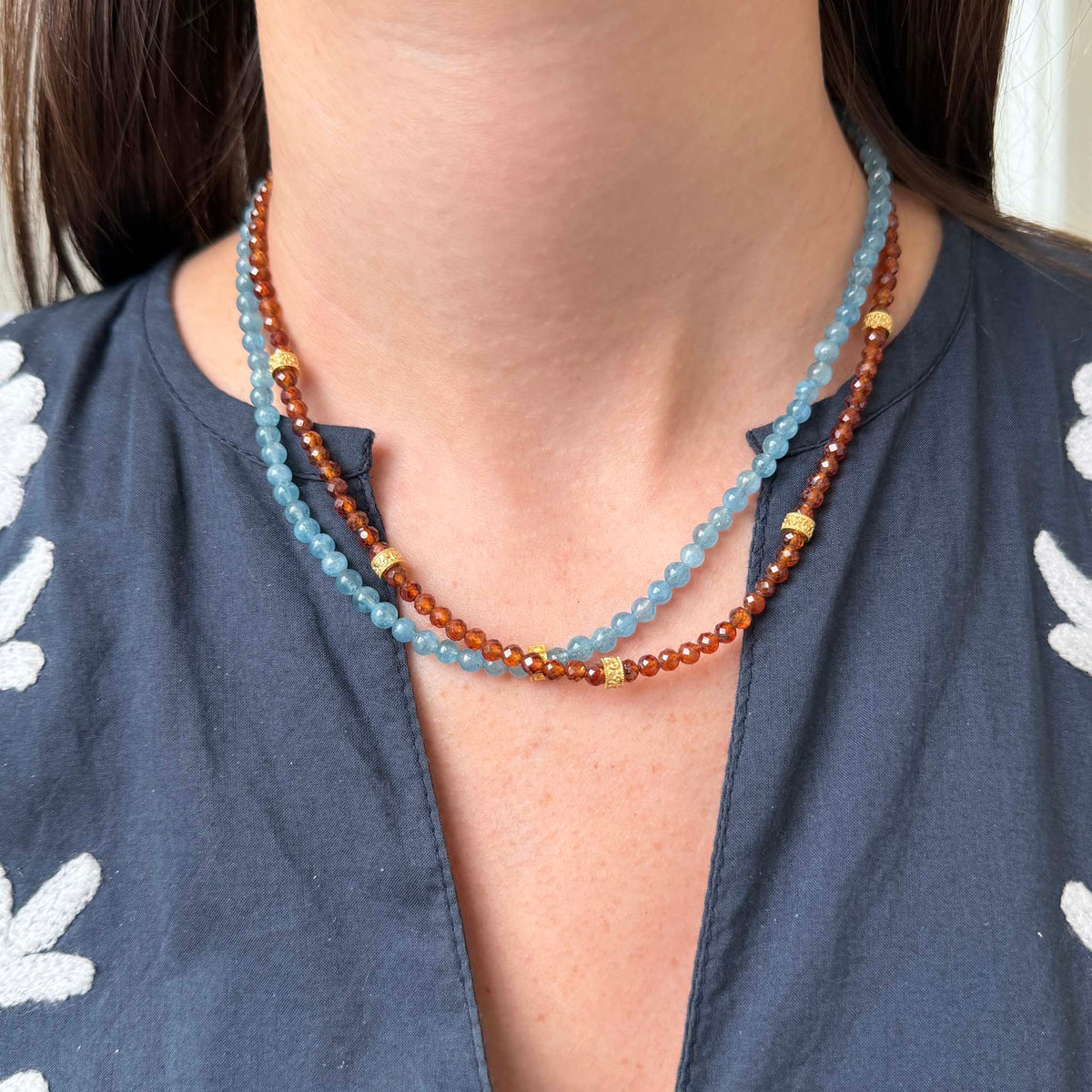 Model wearing a Tippy Stern hessonite garnet necklace with yellow gold rondelles, layered with a blue aquamarine beaded necklace.