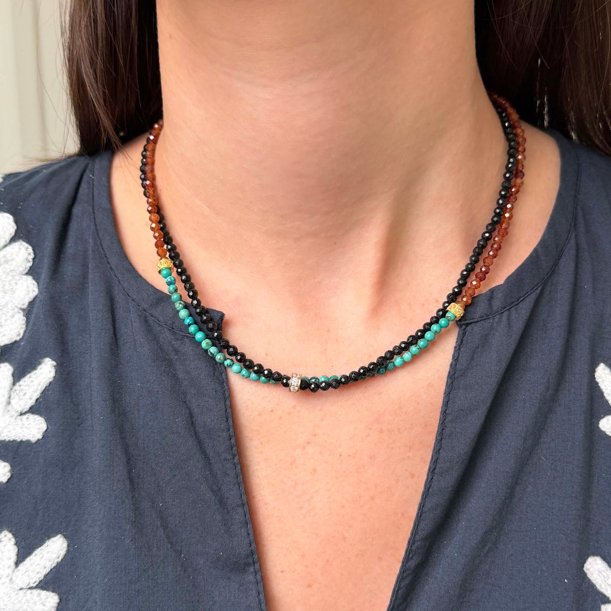 Model wearing a Tippy Stern turquoise and hessonite garnet necklace with yellow gold rondelles, layered with a Tippy Stern black tourmaline necklace with a diamond pavé rondelle.