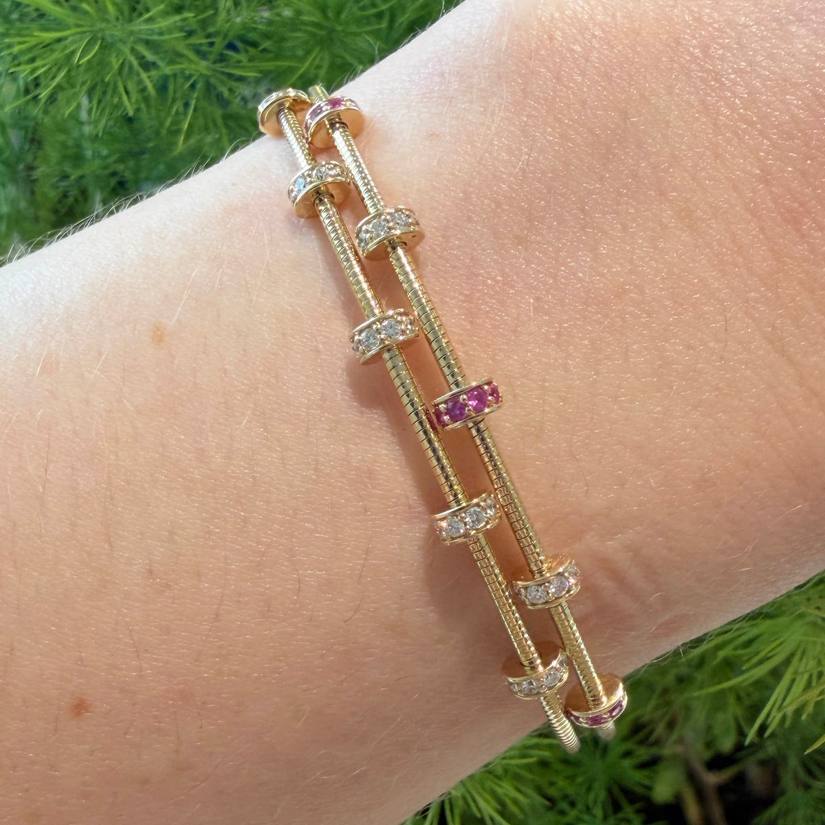 Pink sapphire and diamond rondelle bangle in 14K yellow gold worn on the wrist beside a diamond rondelle bangle.