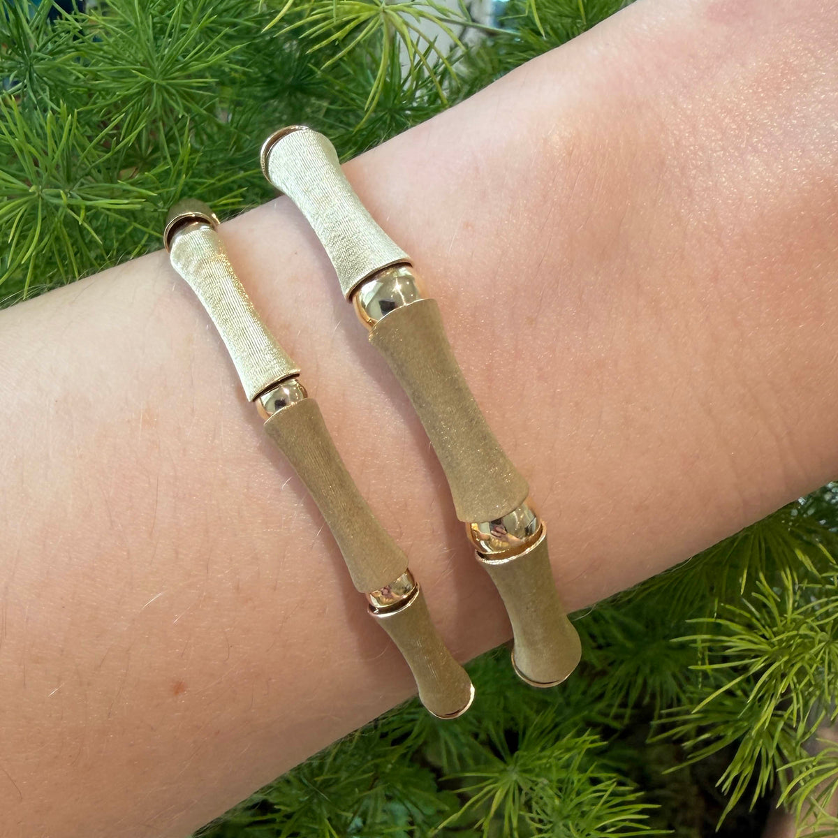Two gold bamboo link bracelets worn side by side, showing their satin-finish links and polished connectors.