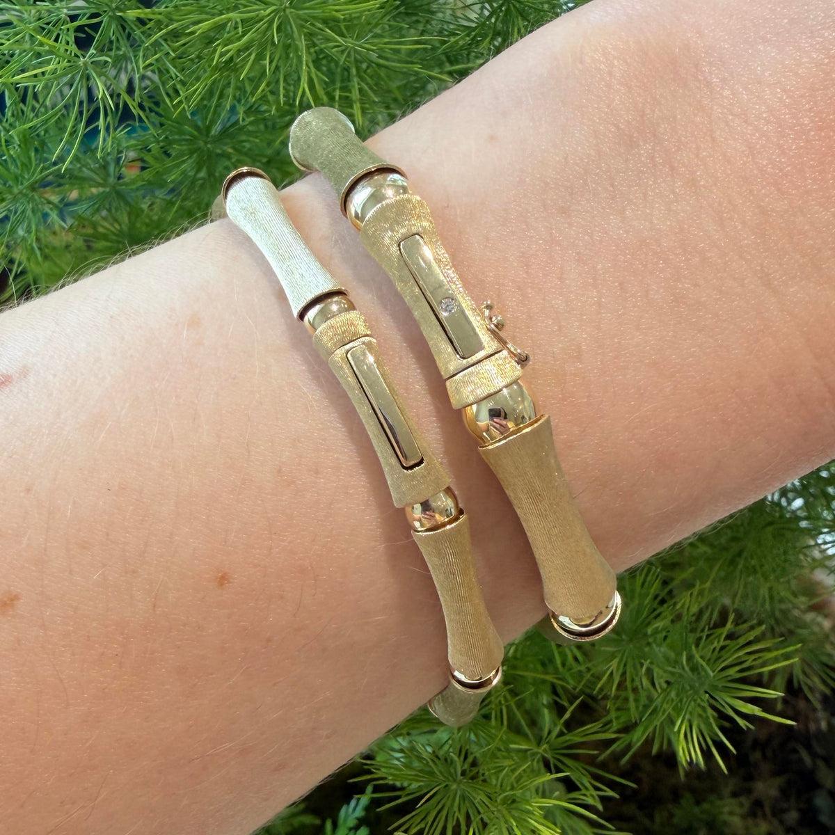 Two gold bamboo link bracelets worn side by side, showing their clasps and contrasting satin and polished finishes.