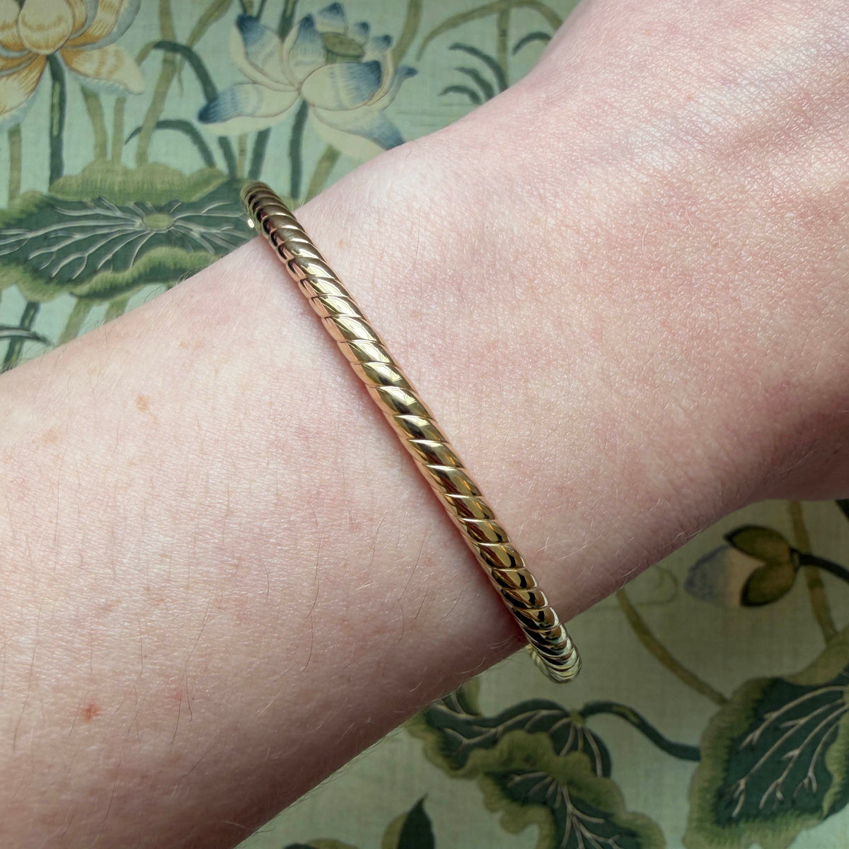 14K yellow gold twisted rope bangle worn on the wrist, showing its slim profile and polished texture.