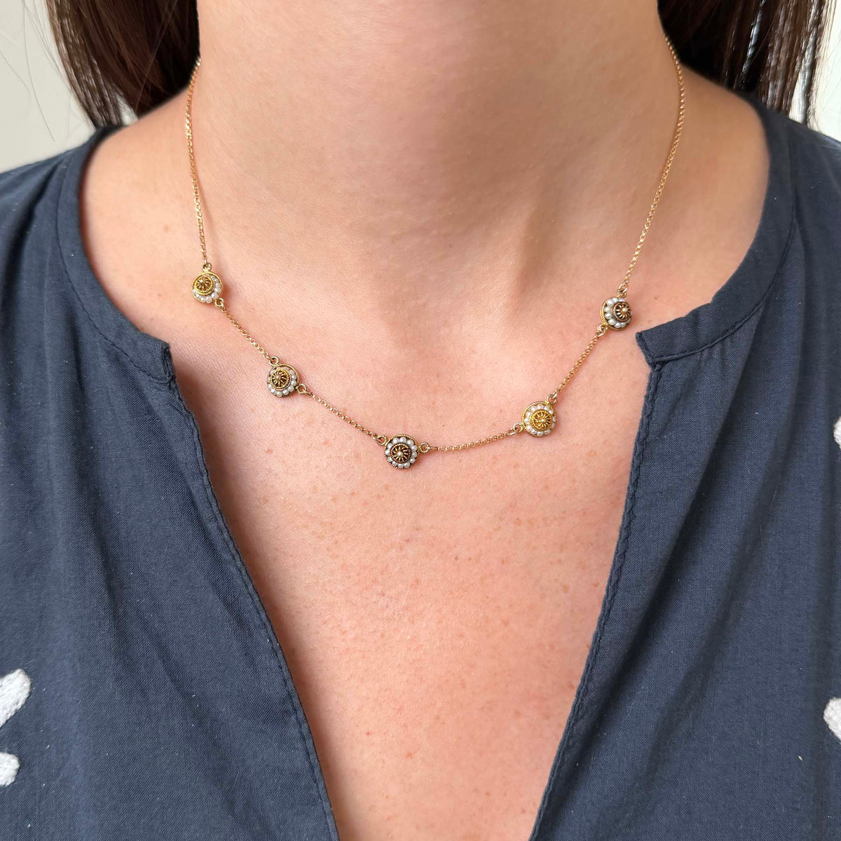 Vintage gold necklace with five seed pearl rosette discs worn around the neck to show its length and scale.