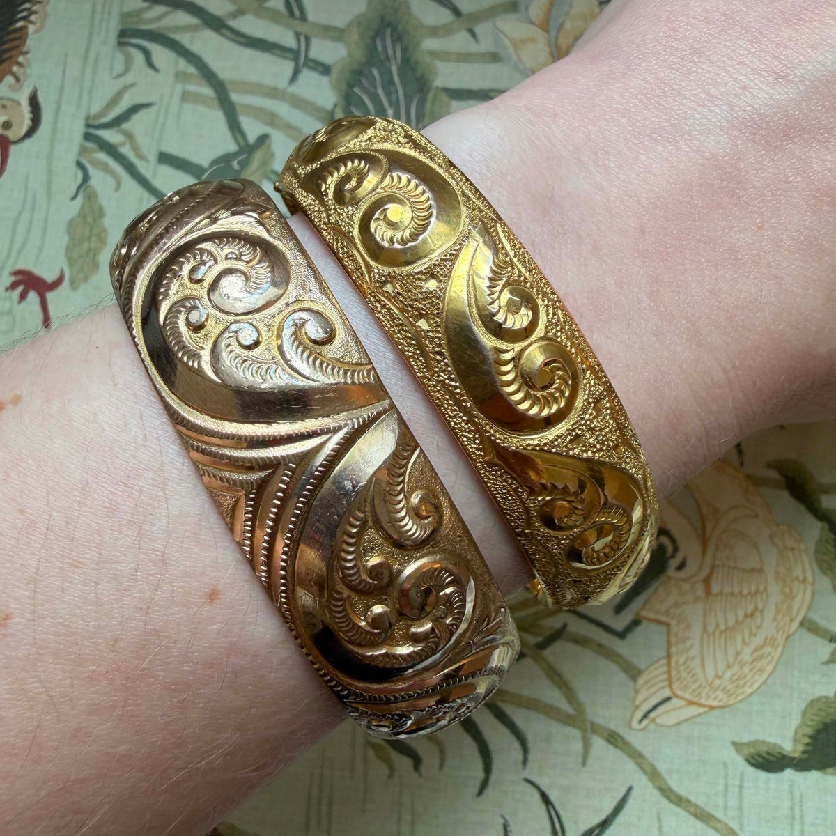 Vintage gold-filled scroll-pattern bangle worn on a wrist beside another engraved bangle.