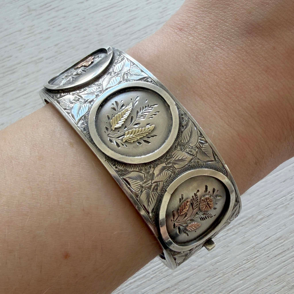 Victorian gold overlay sterling silver wide bangle worn on a wrist, showing three circular floral vignettes.