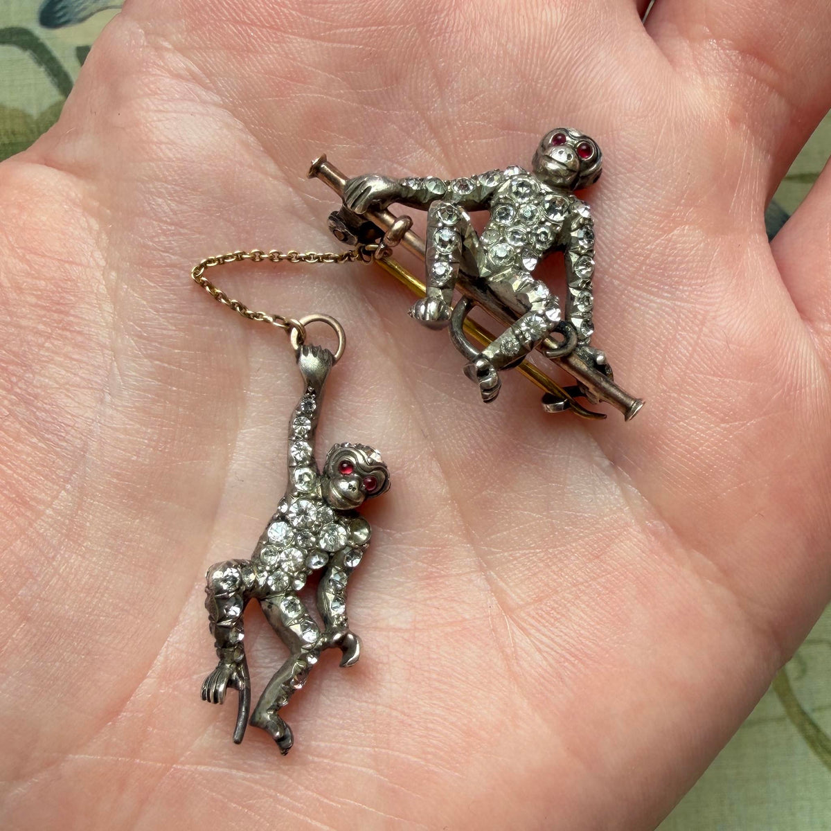 Vintage two-monkey brooch with clear paste stones and red eyes resting in a palm to show its size.