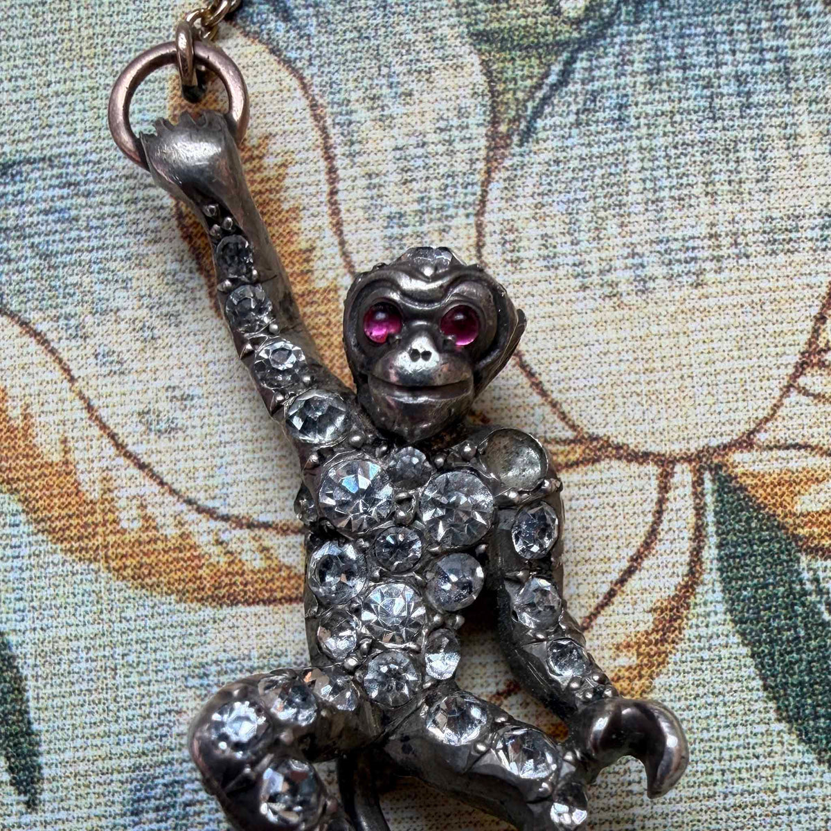 Close-up of the dangling monkey with red paste stone eyes, clear stones, and a missing stone on its shoulder.