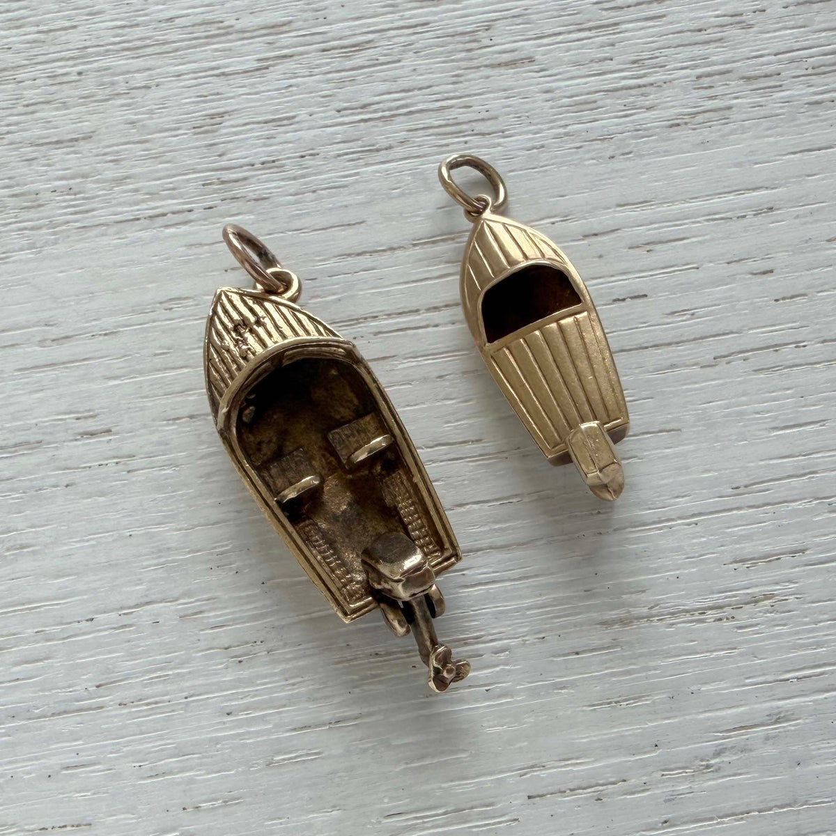Vintage gold speedboat charm beside a larger motorboat charm, showing their decks and cockpits on white wood.