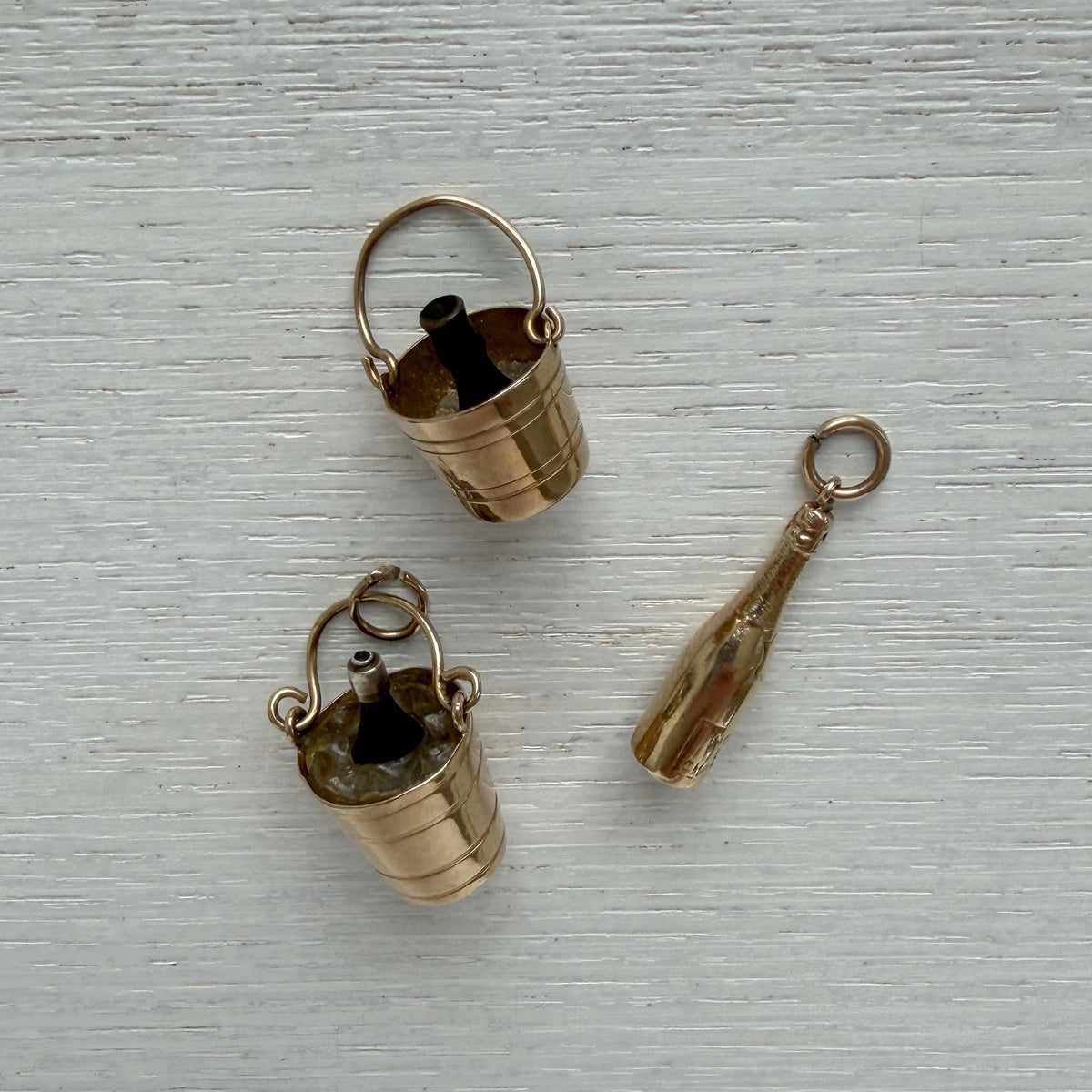 Angled view of two gold champagne bucket charms with black bottles beside a gold champagne bottle charm.