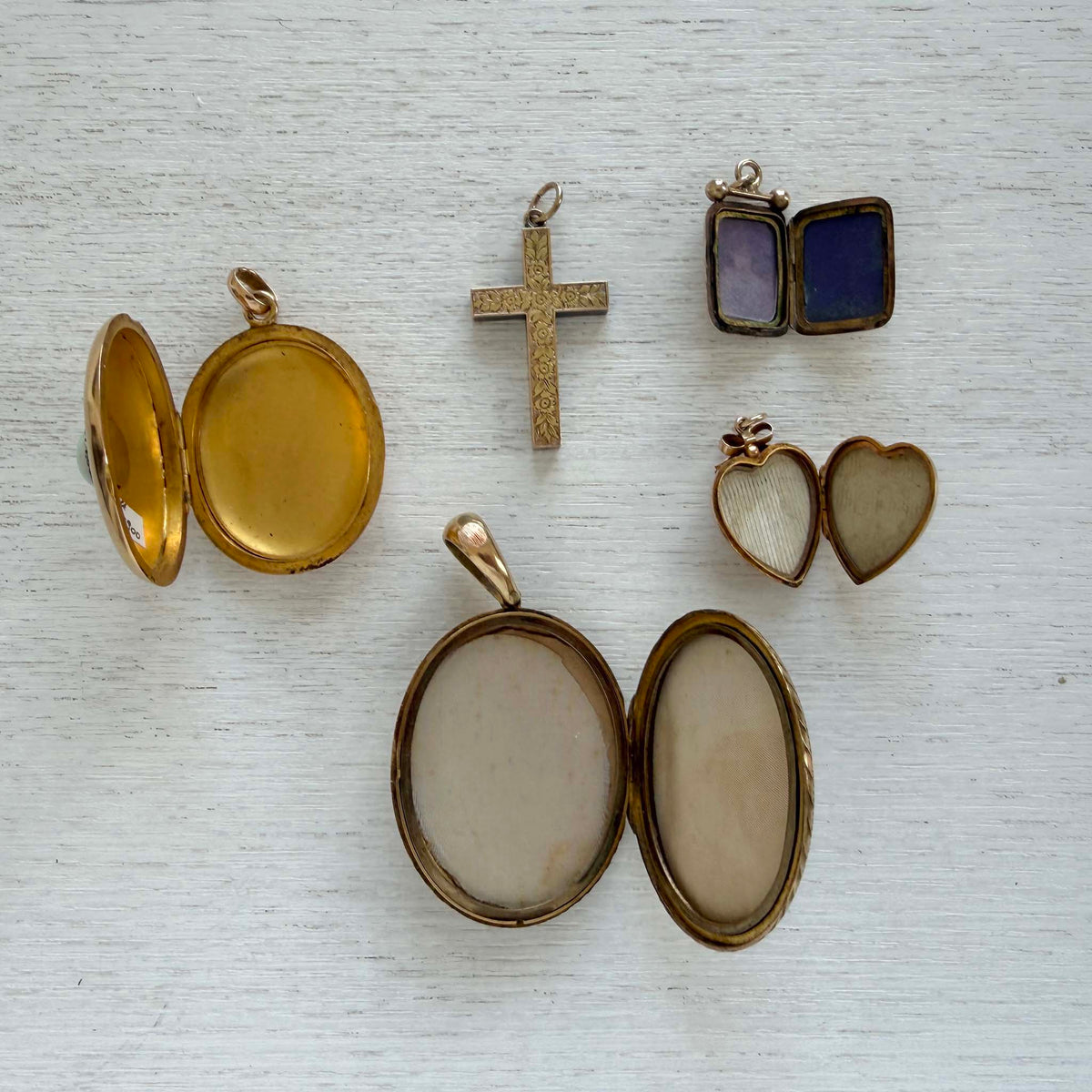 Edwardian heart locket opened to show two heart-shaped photo compartments, displayed alongside other lockets and a cross.