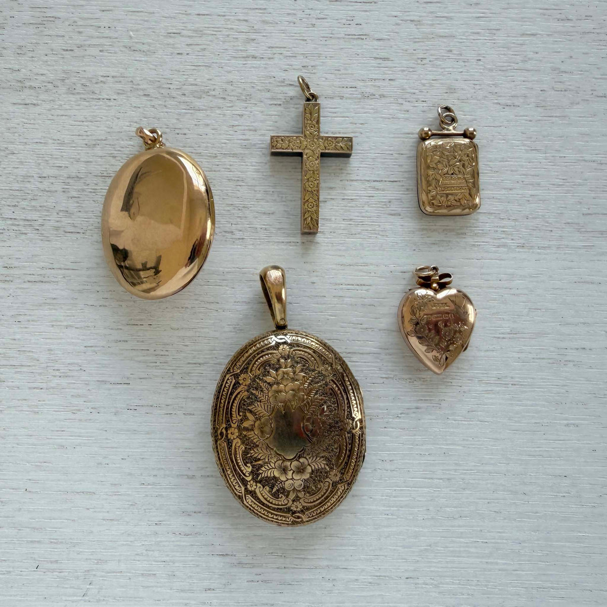 Edwardian heart locket shown back up with floral and bird engraving, alongside other gold lockets and a cross pendant.