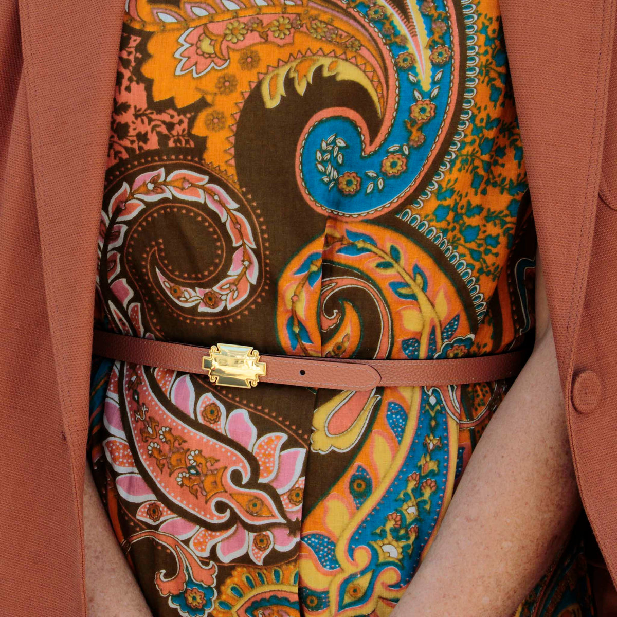 Saddle brown leather belt with a gold-plated plaque buckle, worn over a paisley print dress and a dusty rose blazer.